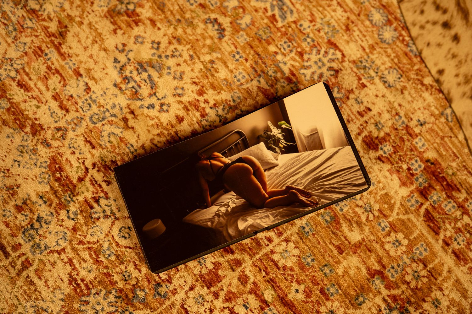 A photograph lying on an ornate golden floral patterned rug showing a dimly lit bedroom scene.
