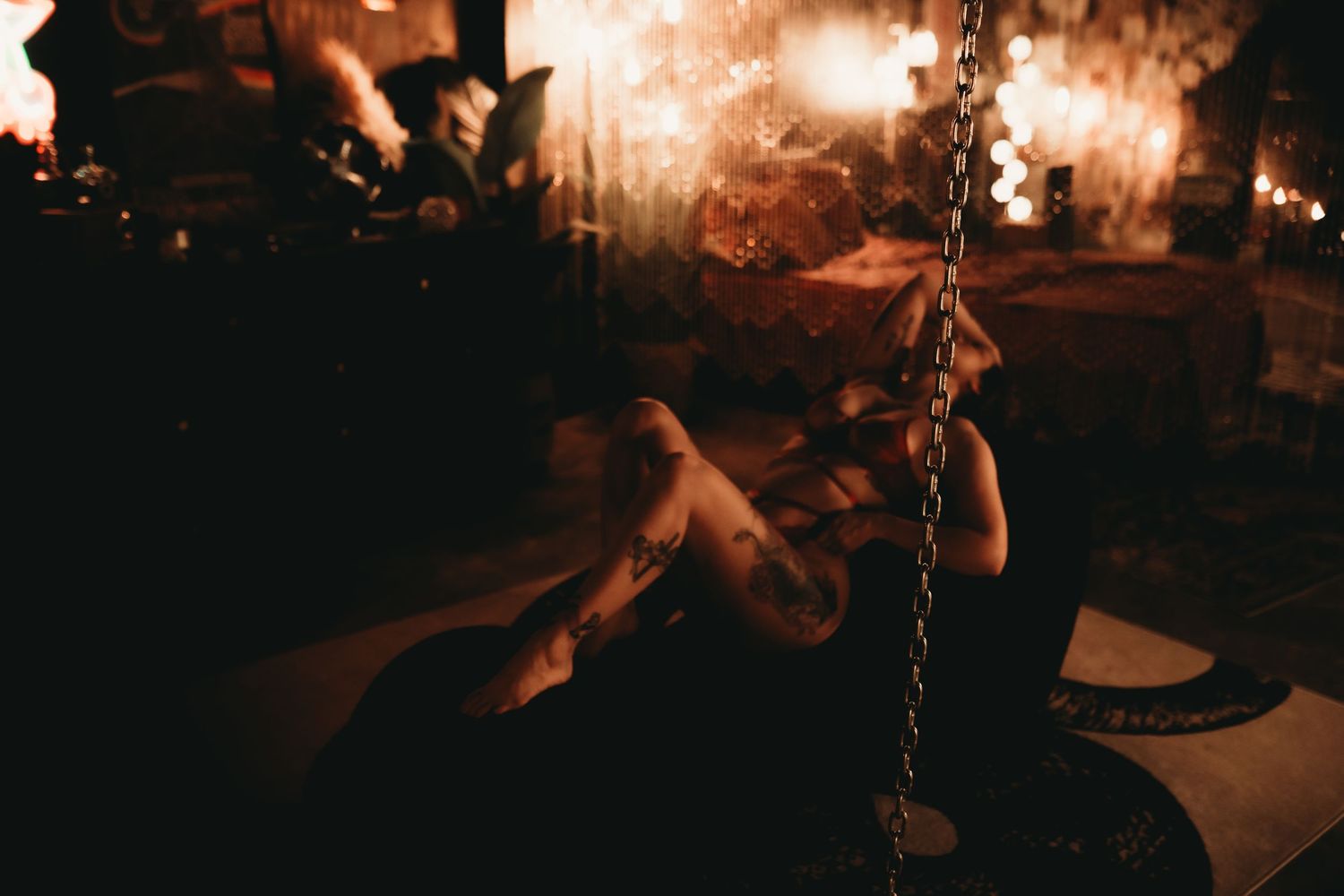 Person sitting on a swing in a dimly lit, warmly glowing room with bokeh lights in the background.