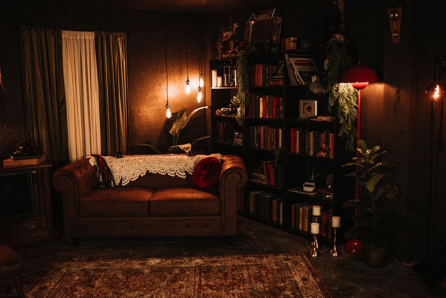 Cozy dimly lit reading room with leather sofa, tall bookshelf, warm Edison bulb lighting, and rich wood-paneled walls.