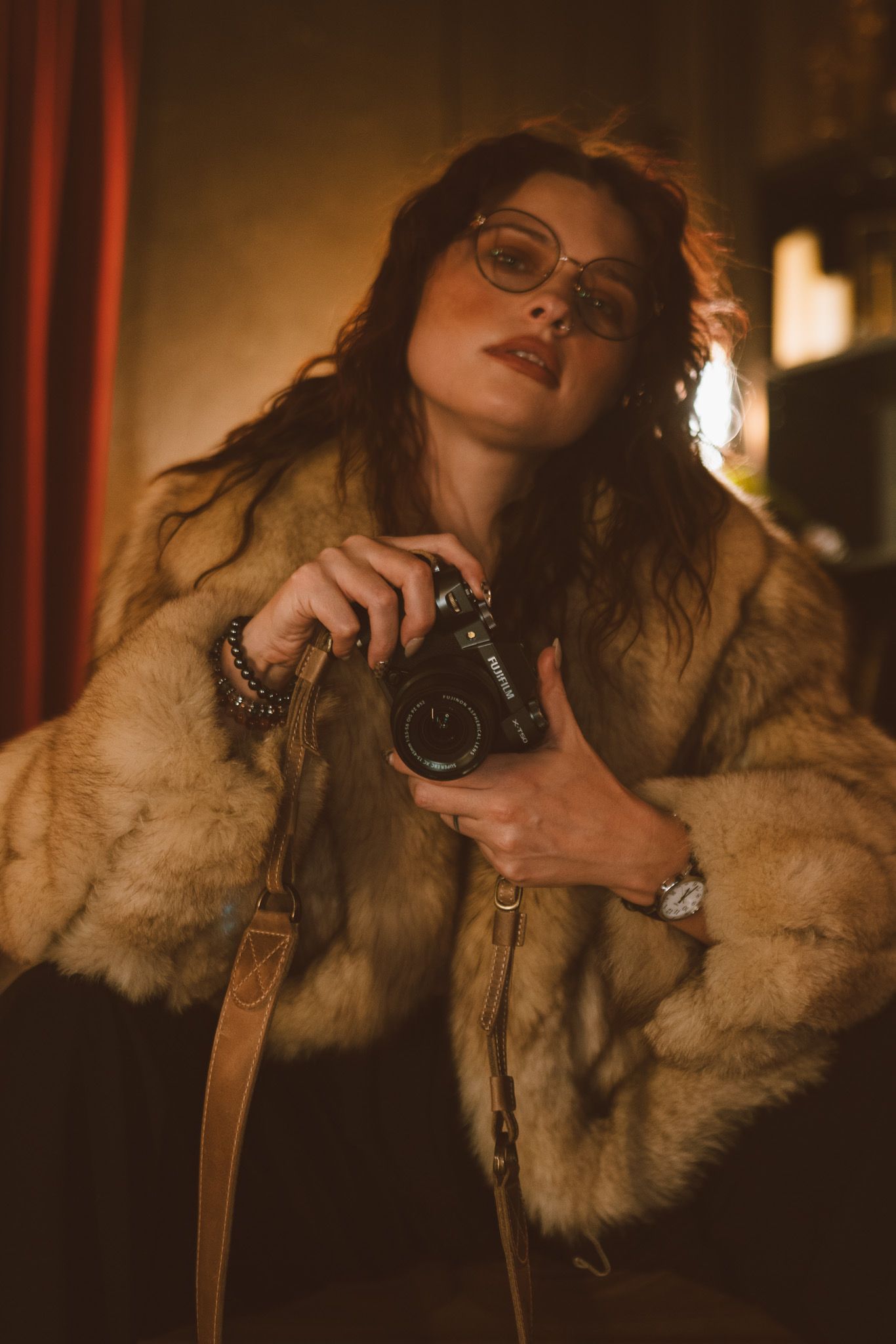 Artistic portrait series in warm lighting showing a person wearing a fur coat and glasses against a dark background.