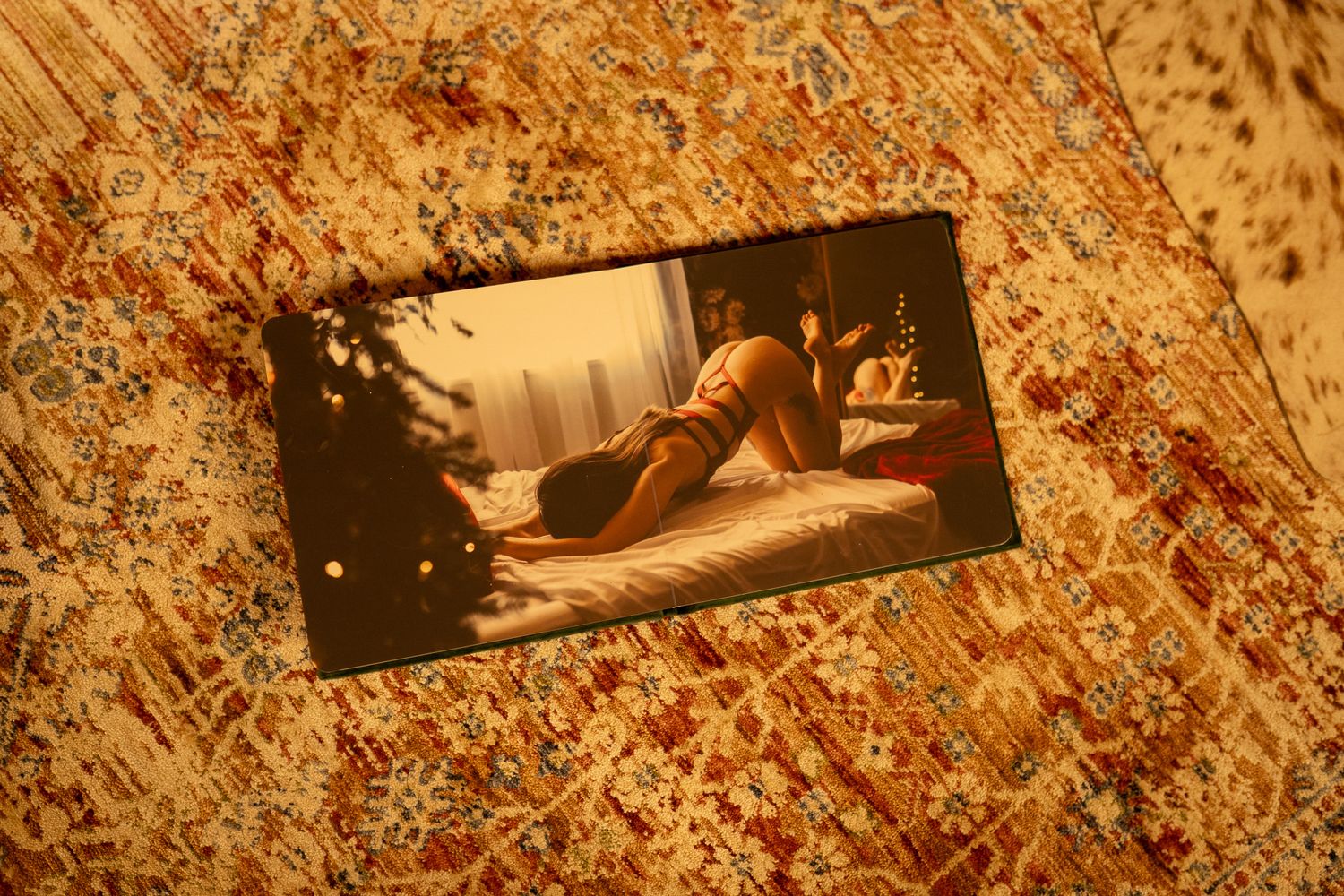 A photograph of a person reclining on a bed, displayed on a vintage floral patterned carpet.