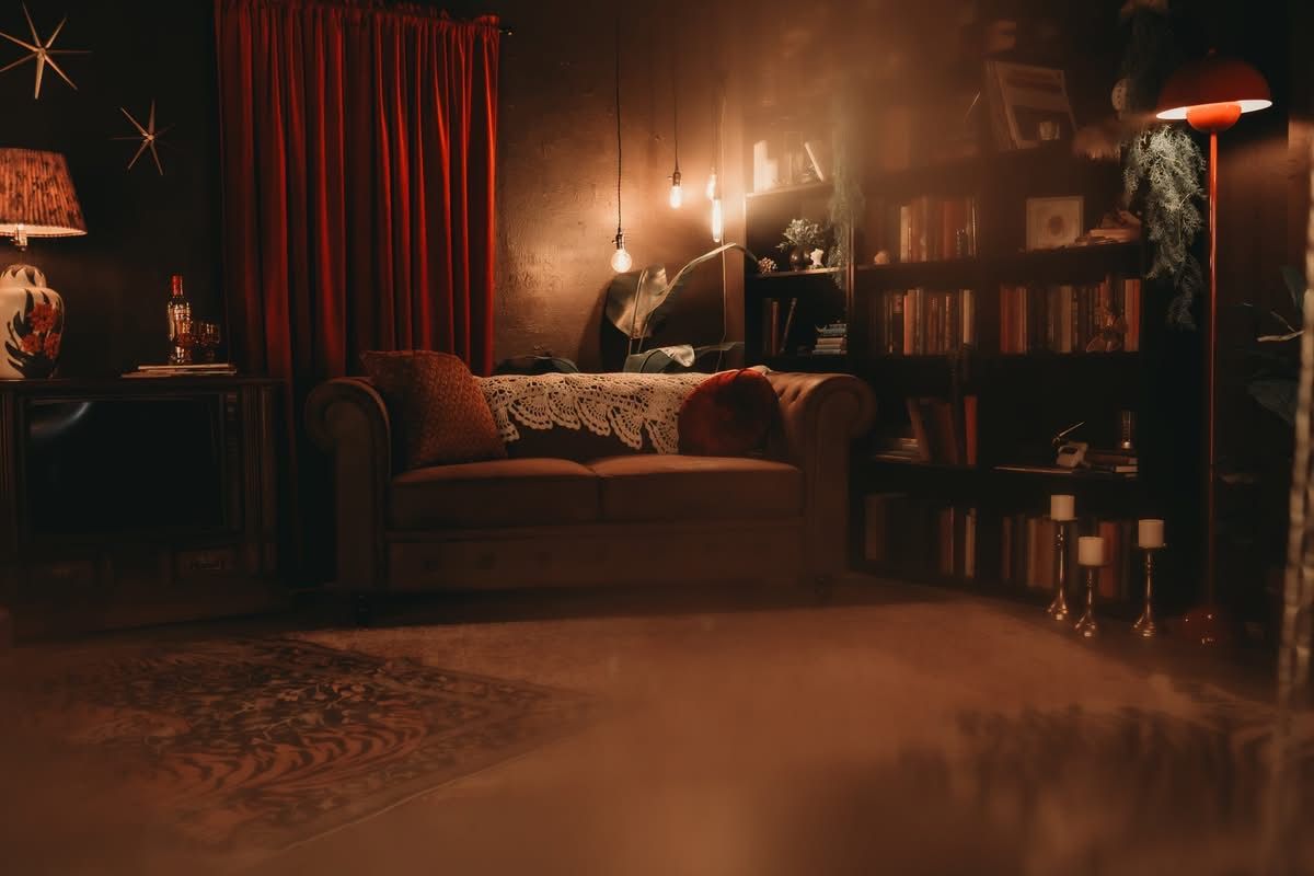 Moody vintage living room with red curtains, leather sofa, bookshelf, and warm ambient lighting.