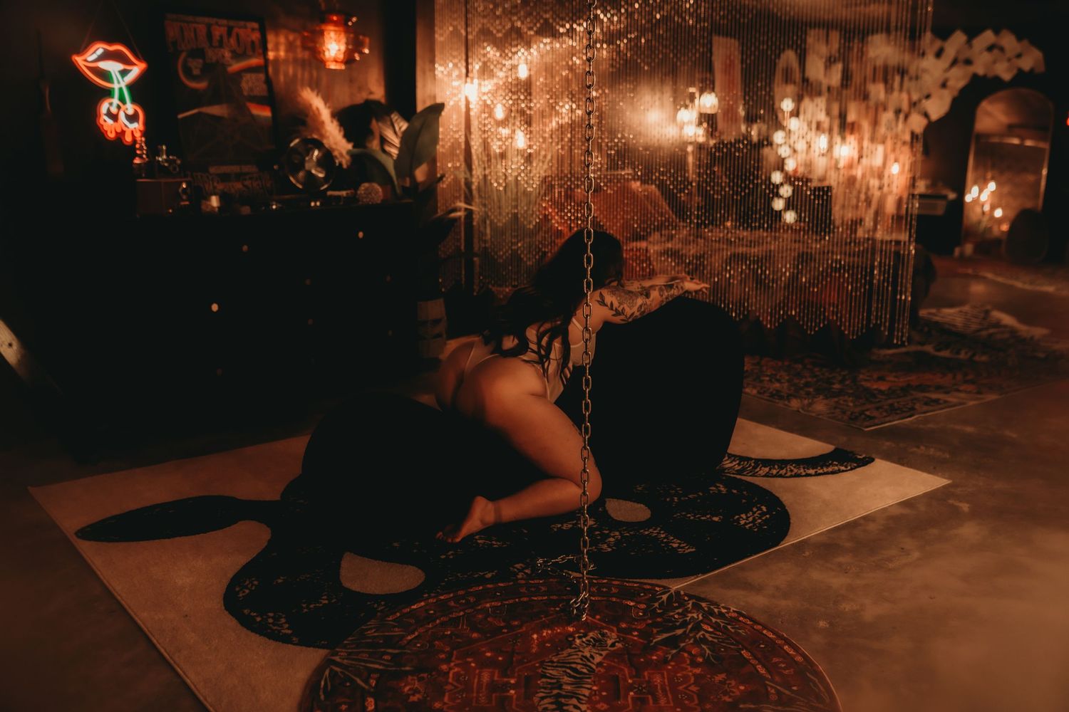 Dimly lit bohemian room with warm amber lighting, decorative rugs, and a person posing dramatically on the floor.
