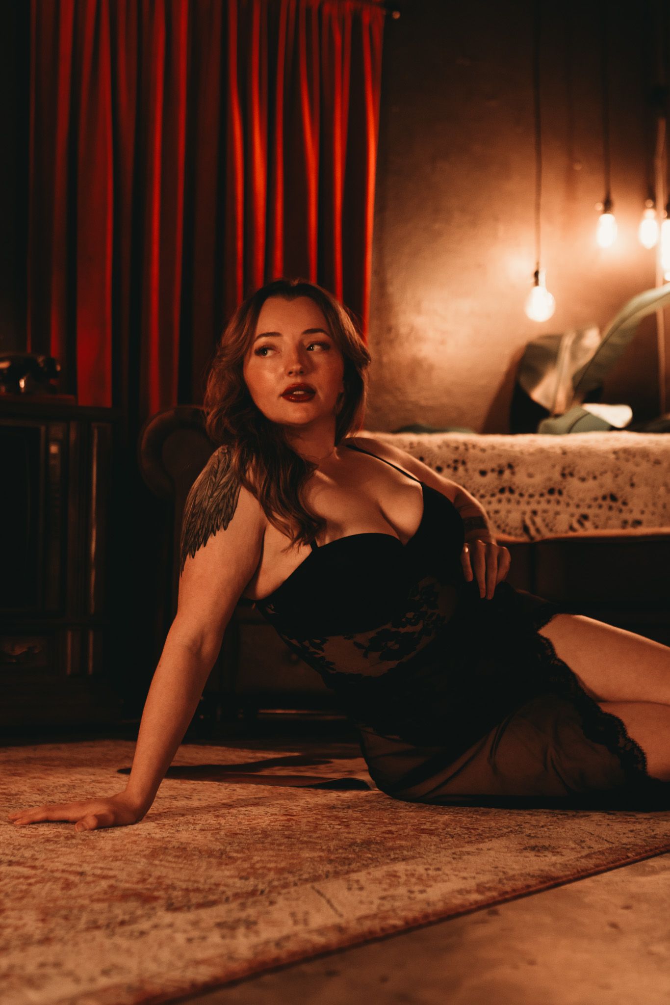 Moody boudoir photography series showing a figure in black lingerie on carpet in dramatic low lighting.