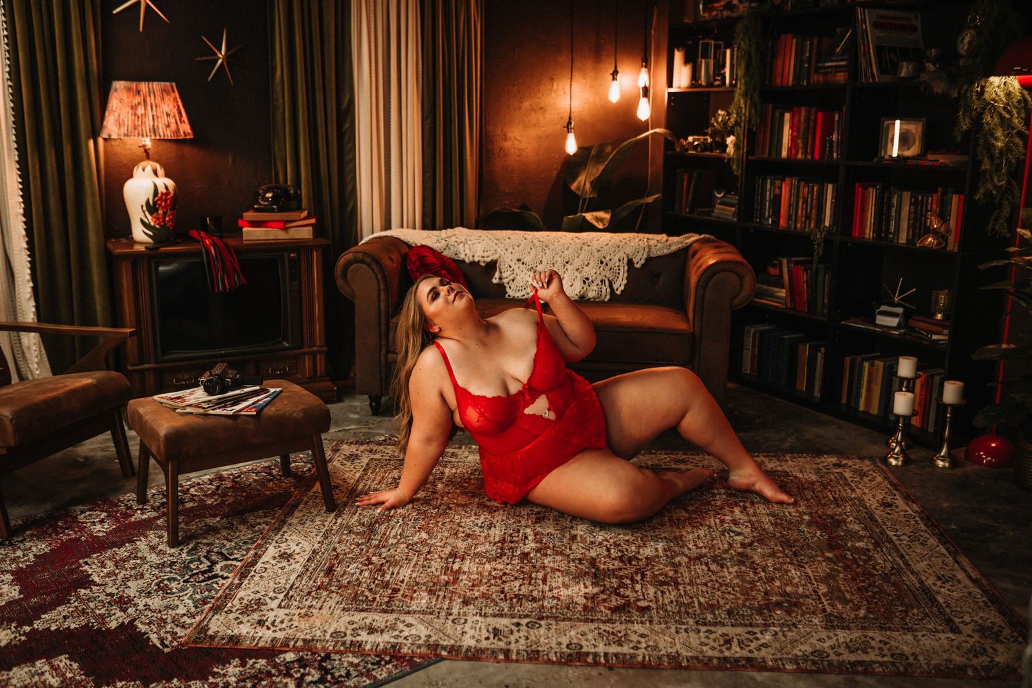 A cozy library room with warm lighting features a vintage rug, bookshelves, and someone in red lounging on the floor.