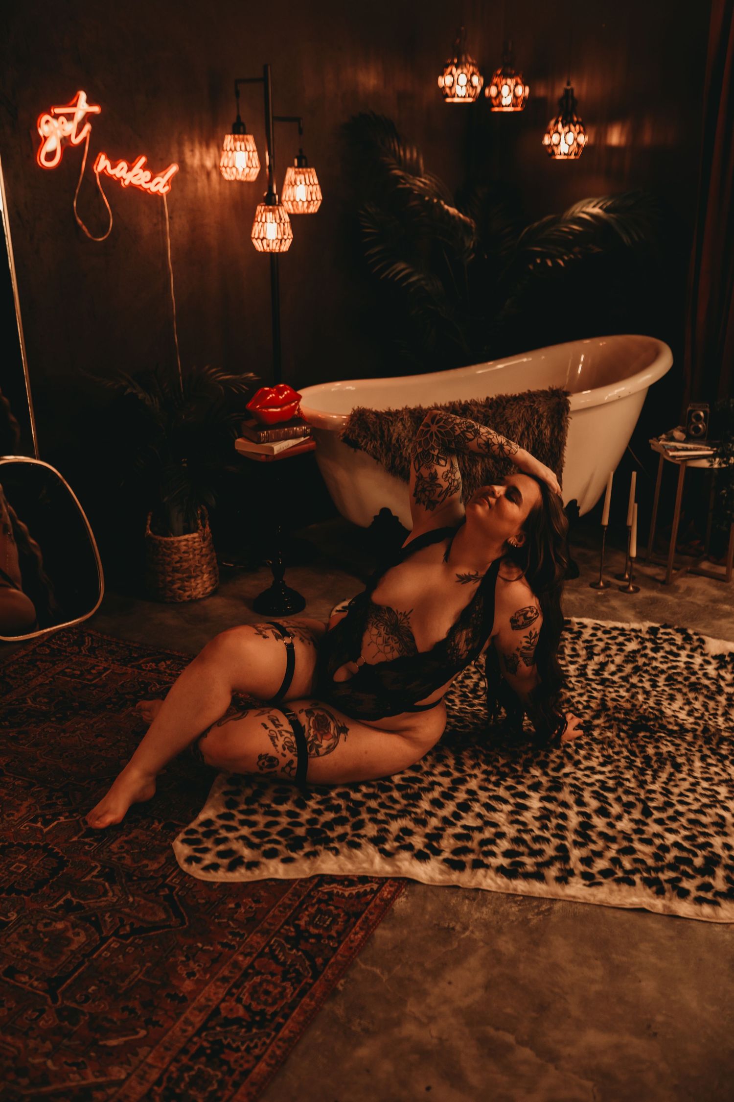 Woman in black lingerie posing on leopard print rug near vintage bathtub with warm ambient lighting.