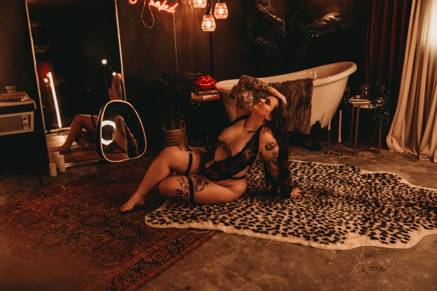 A woman in black lingerie poses on a leopard print rug in a dimly lit, moody room with candles and a bathtub.