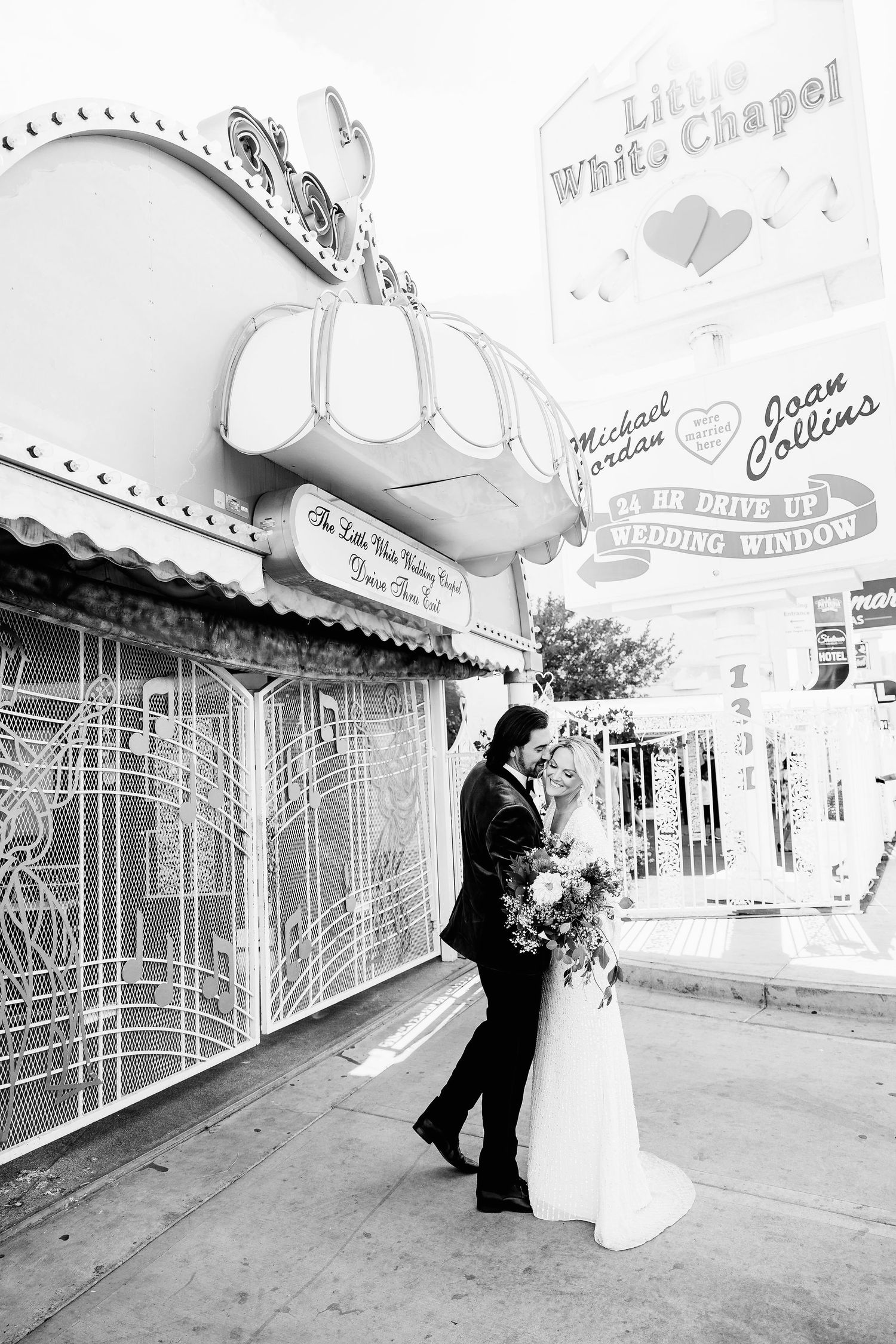 Wedding couple poses for romantic photos outside a vintage-style chapel with retro signage.