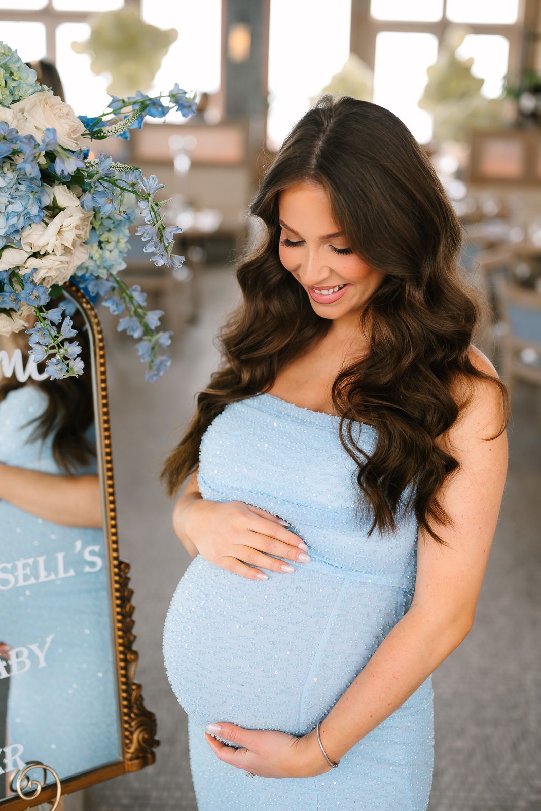 Expectant mother in light blue fitted dress smiles while cradling baby bump photographed by a New Jersey event photographer.