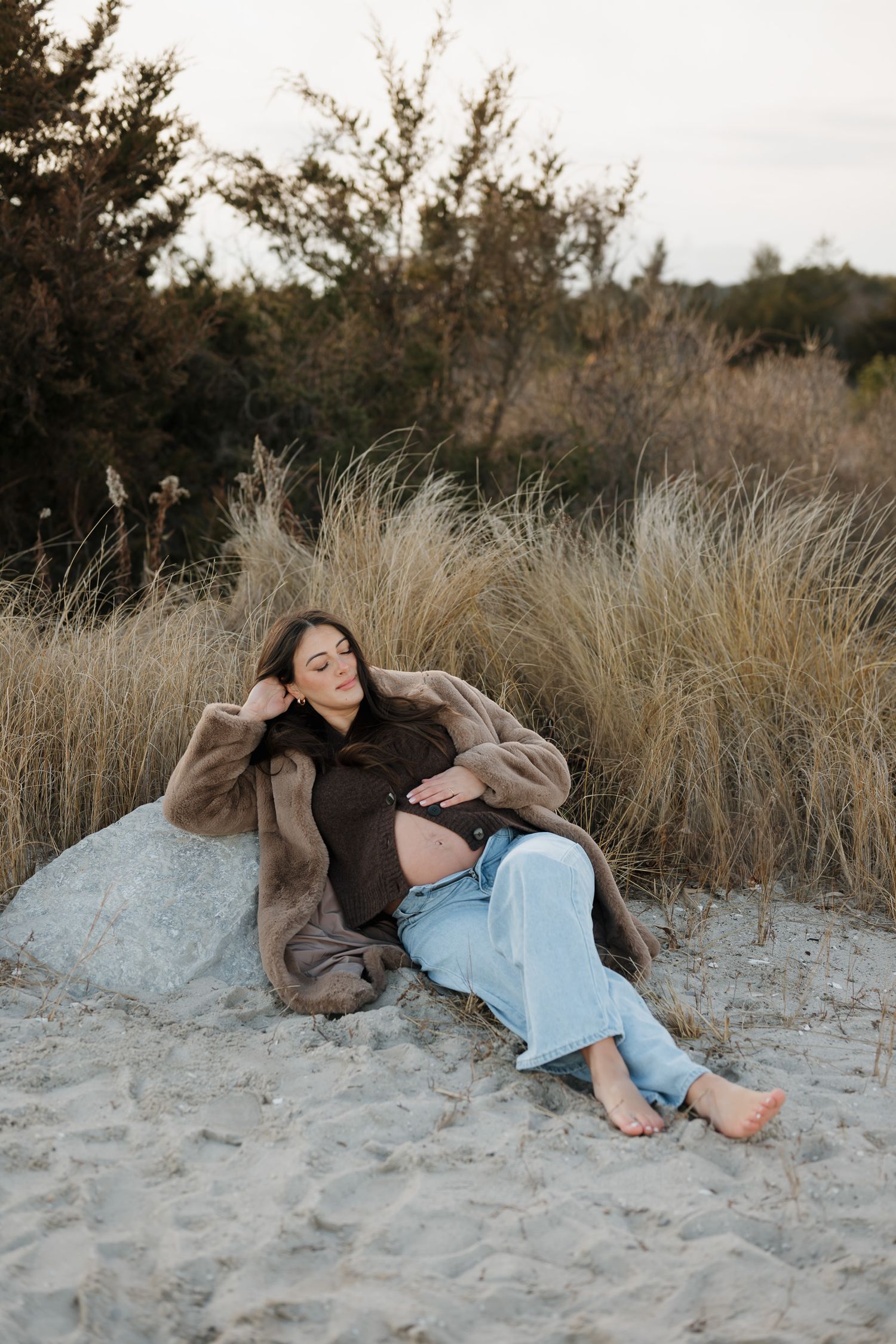 A couple relaxes together on a sandy beach surrounded by tall beach grass during golden hour.