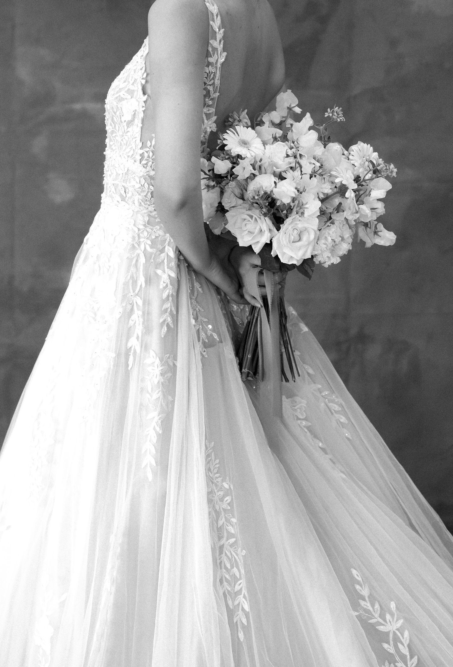 Elegant white wedding dress with delicate floral lace details and flowing tulle skirt captured in black and white photography.
