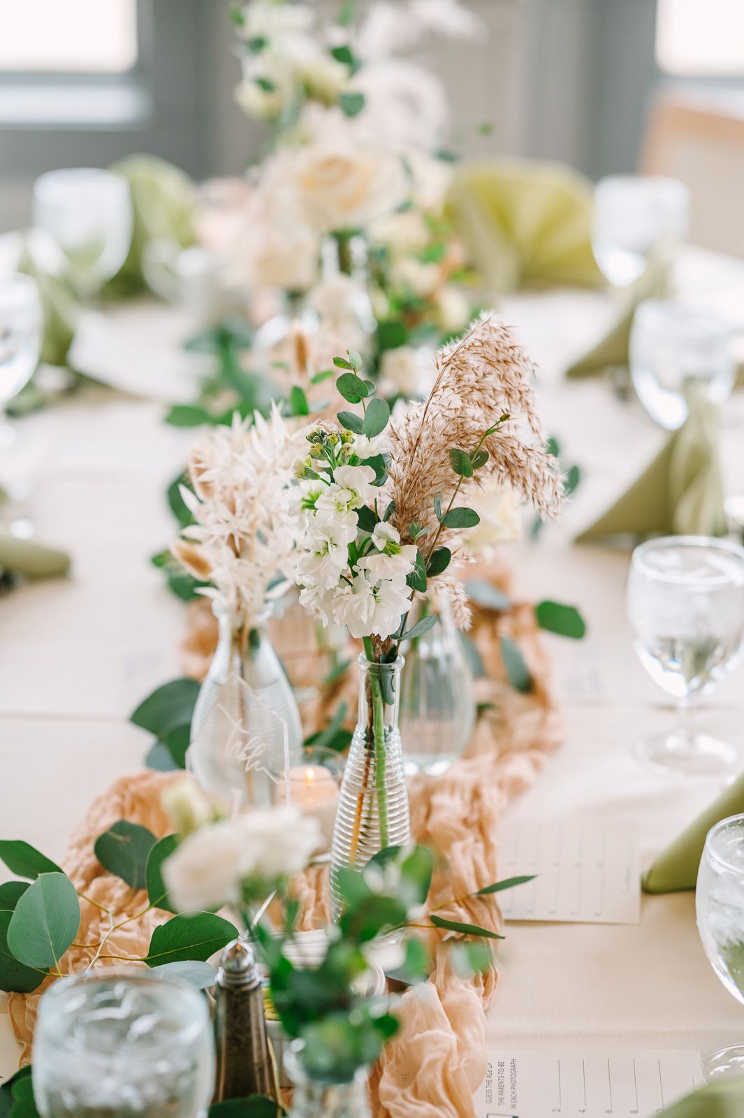 Elegant wedding reception table decorated with white floral centerpieces, eucalyptus greenery, and glowing candles.