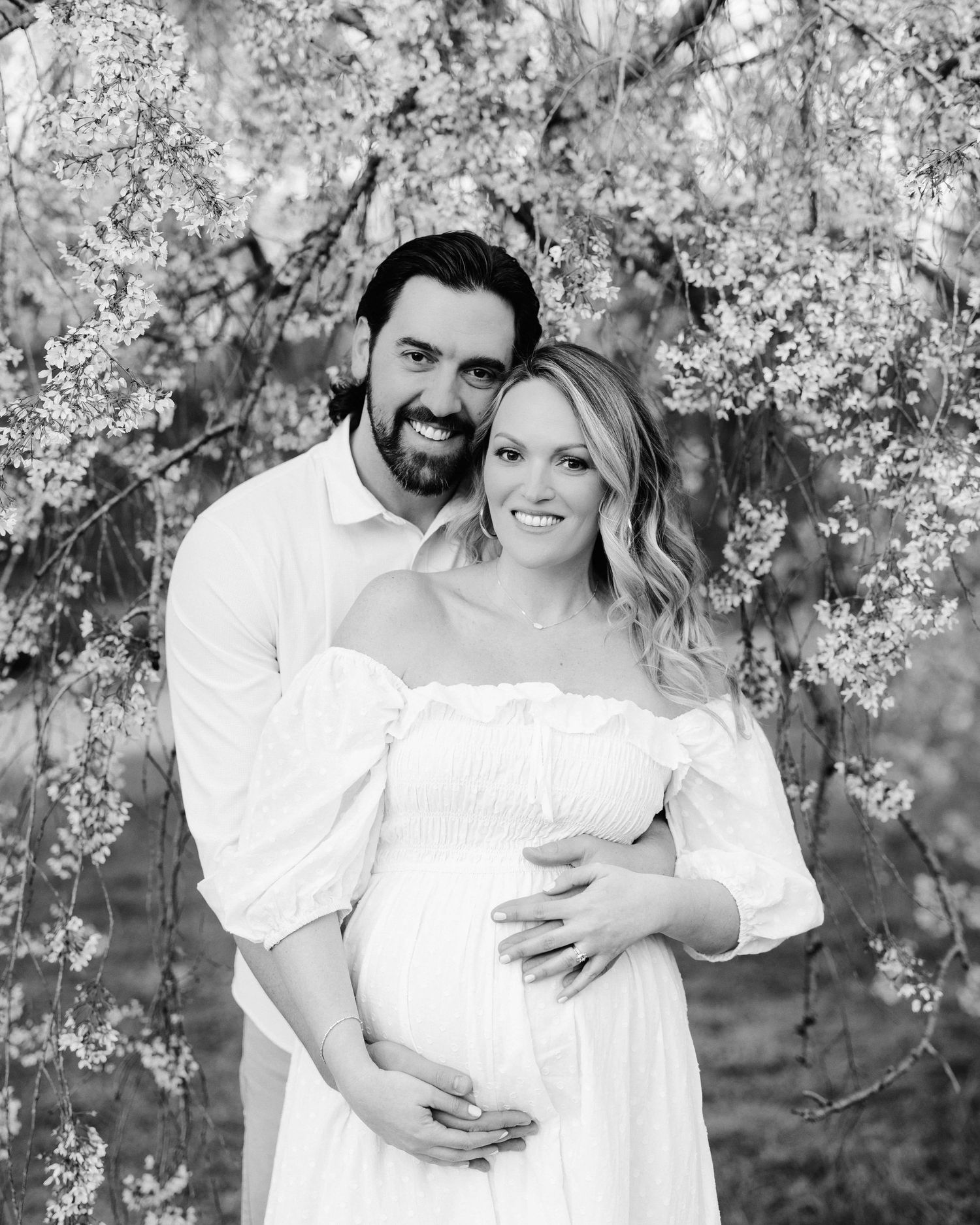 Romantic maternity photos of a couple embracing under blooming cherry blossom trees.