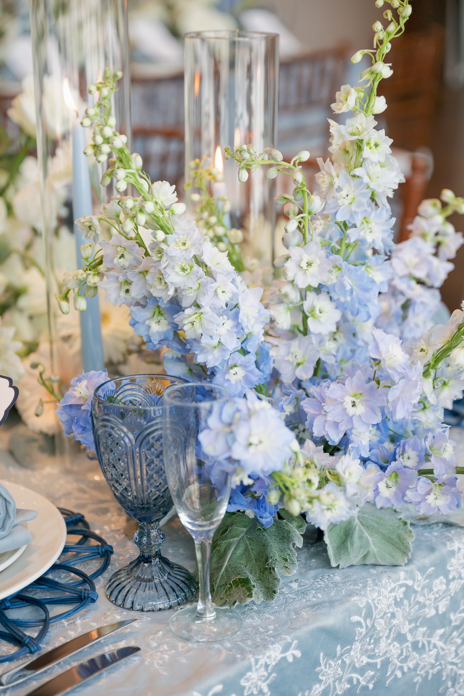 Elegant table setting with blue delphinium flowers and crystal glassware arranged for a formal dining occasion.
