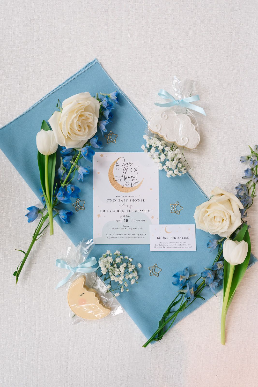 Event invitation suite in dusty blue with white roses and baby's breath flowers arranged on light background.