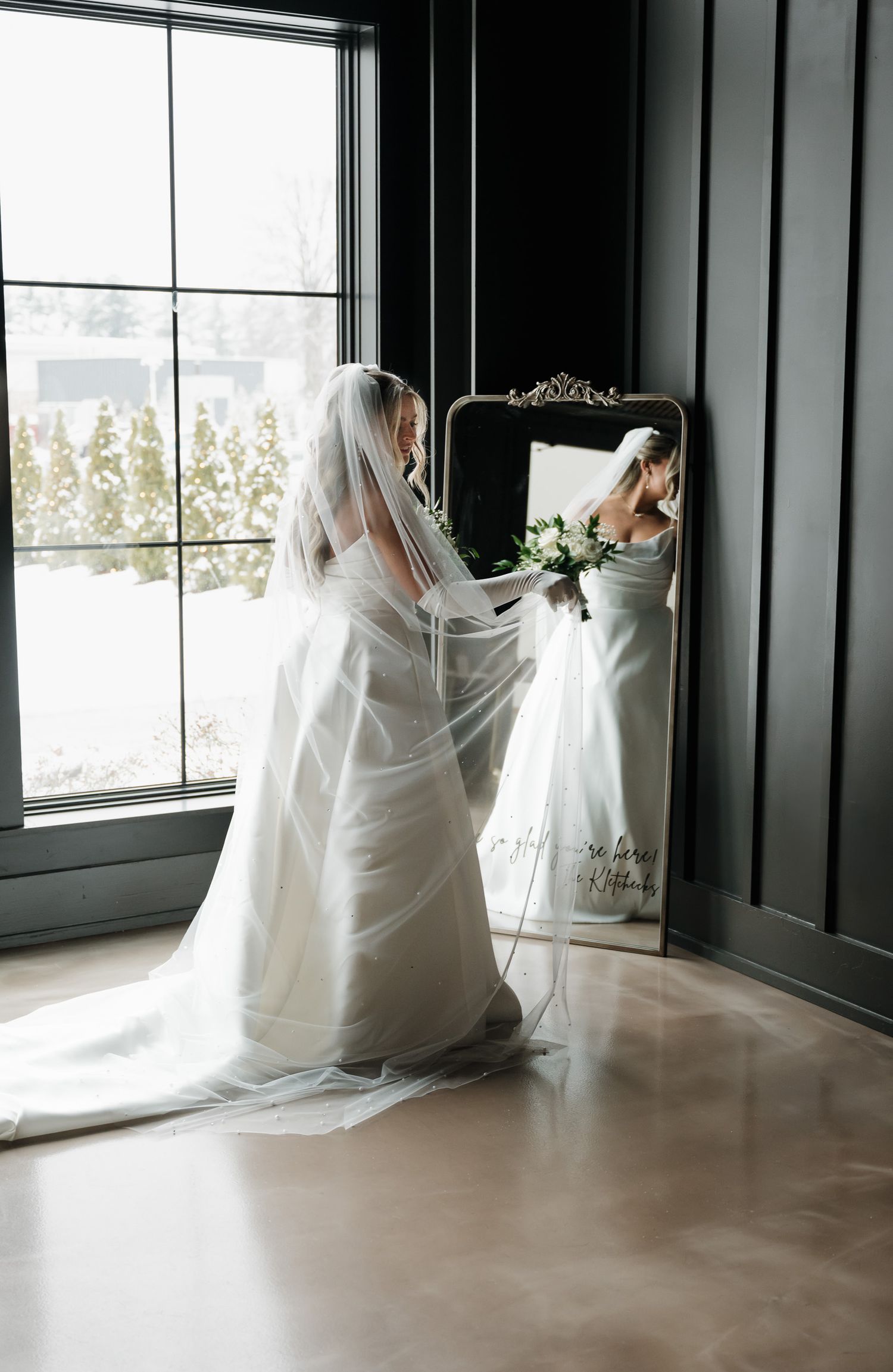 A series of flowing white wedding dresses displayed in a room with dark walls and large windows creating an ethereal effect.