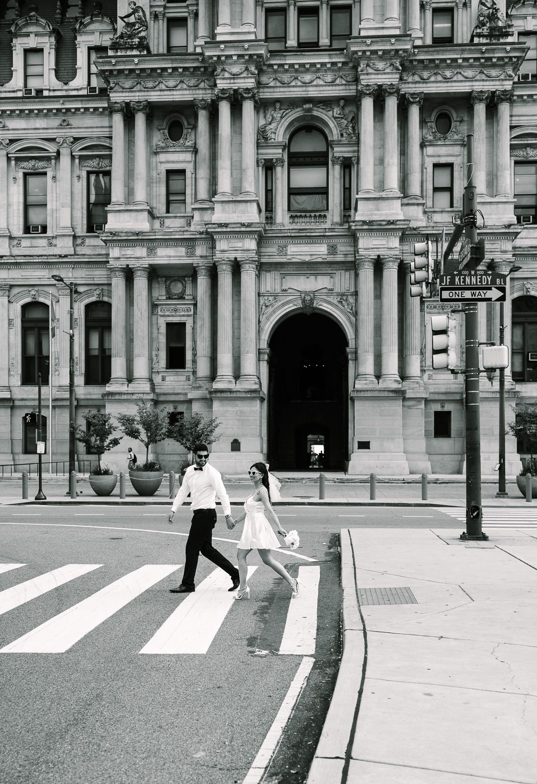 A couple crossing a crosswalk in front of city hall in black and white photography taken by a New Jersey photographer.