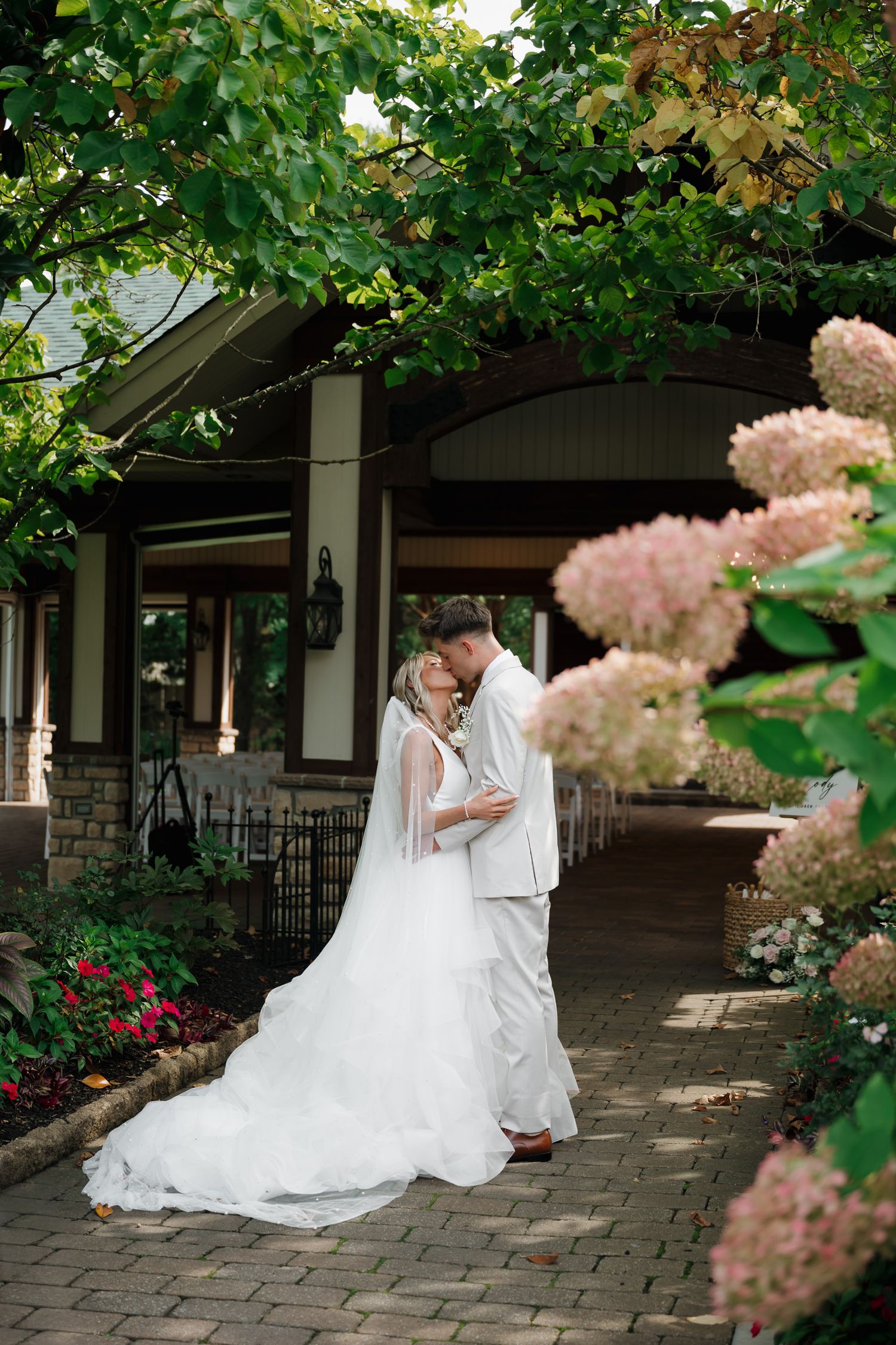 A South Jersey wedding photo series showing a couple in white attire embracing on a stone patio with pink flowers in the foreground.