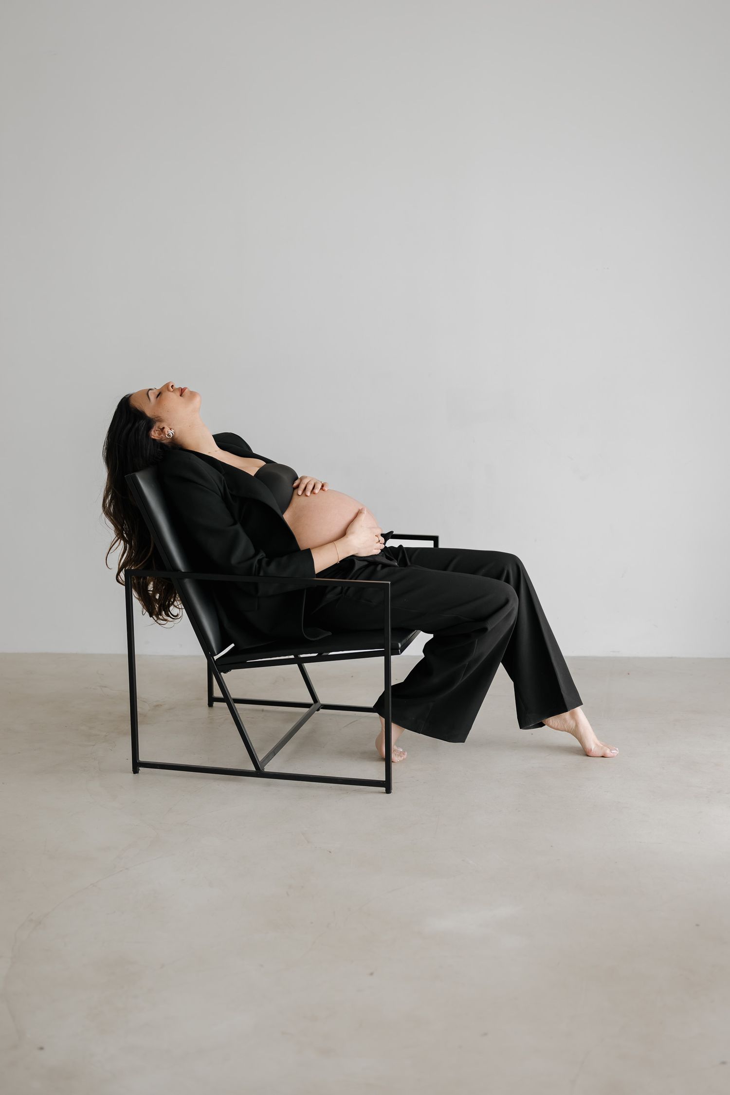 A series of minimalist photographs showing a person in black clothing reclining on a modern lounge chair against a white wall.