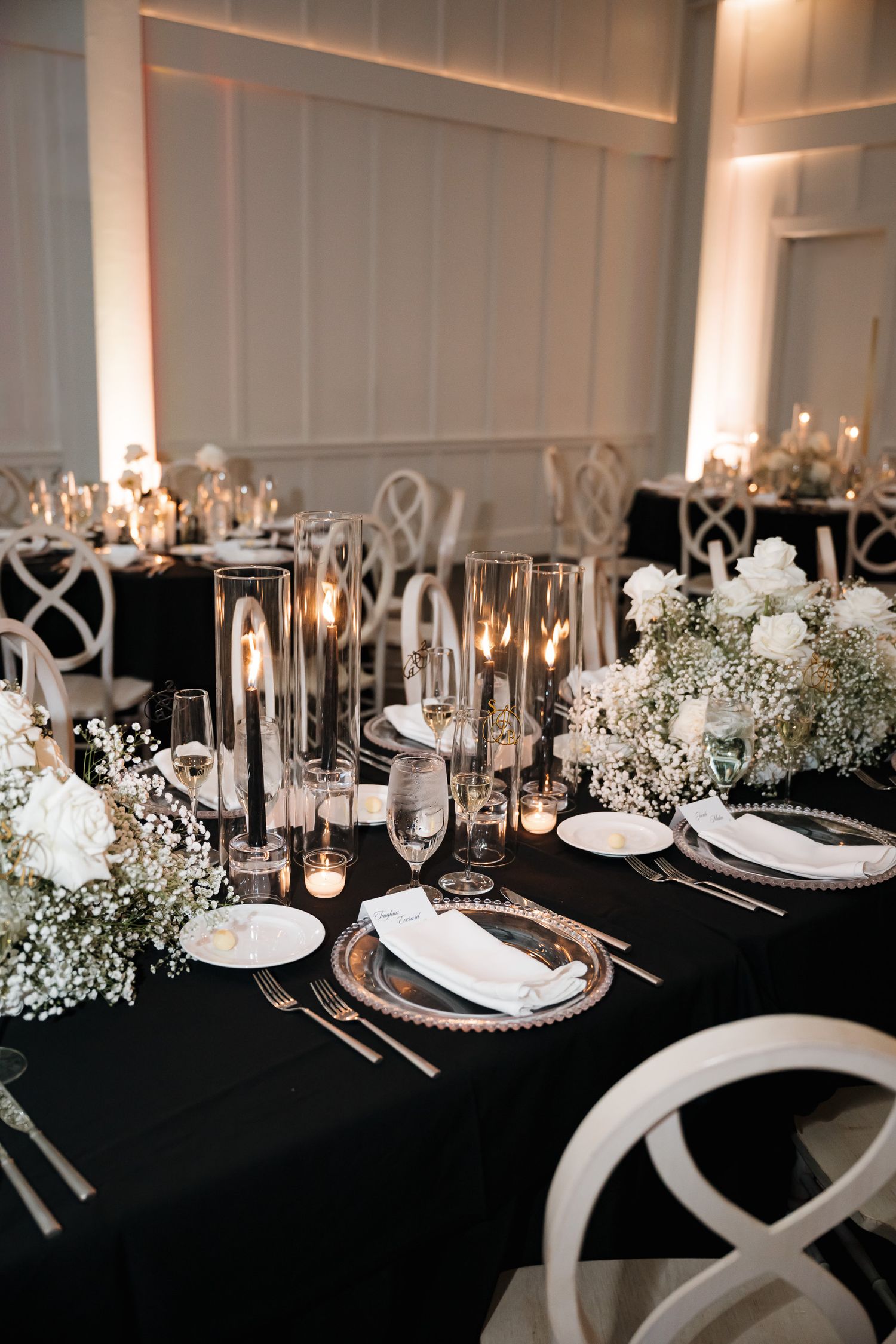 Elegant wedding table setting with black tablecloth, white chairs, candlelight and baby's breath floral arrangements.