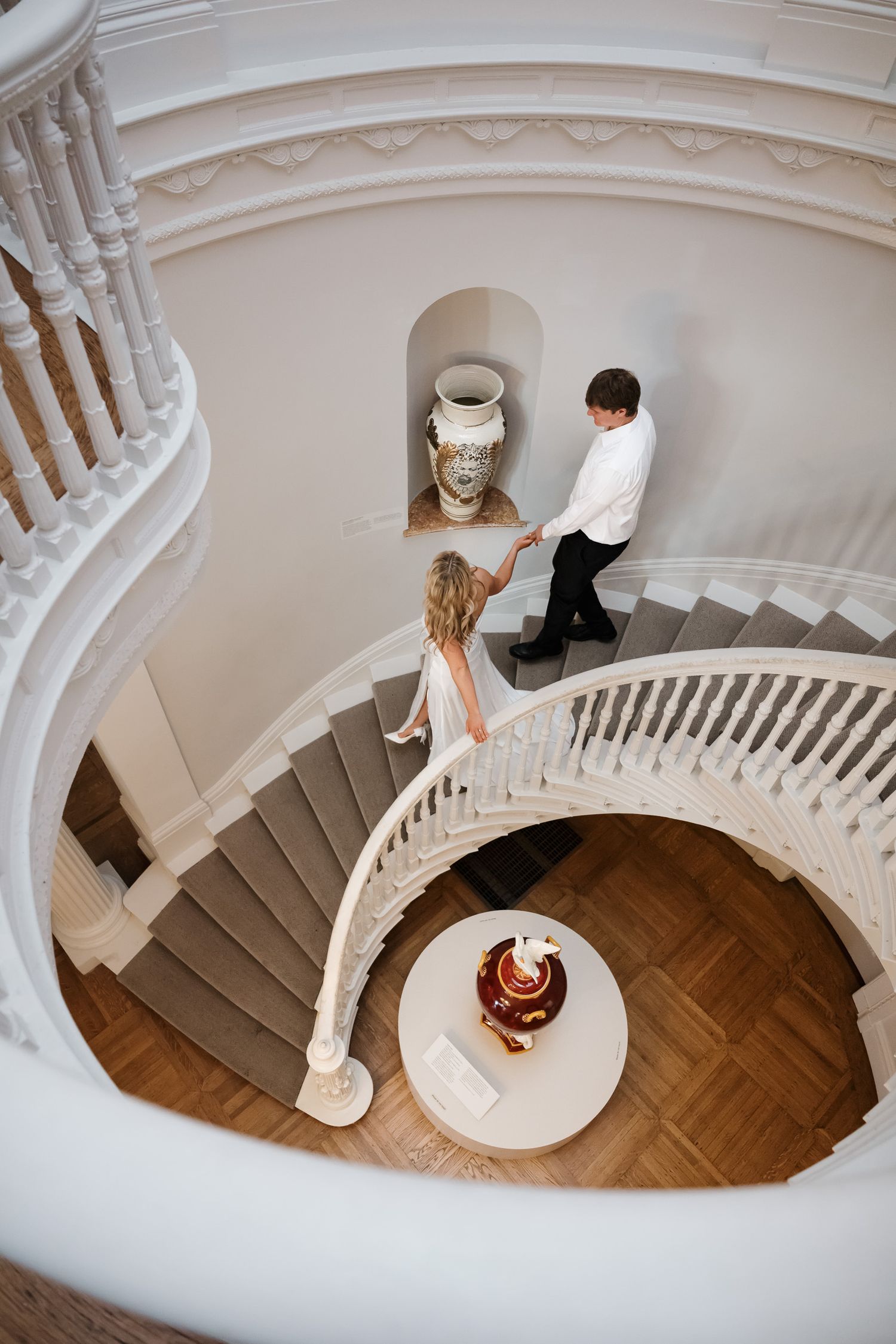 Aerial view of an elegant spiral staircase with white railings and wooden floors in a classical building interior.