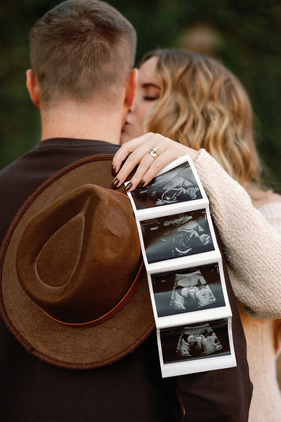 A couple embraces while holding ultrasound photos, with a brown cowboy hat visible in the romantic pregnancy announcement in New Jersey.