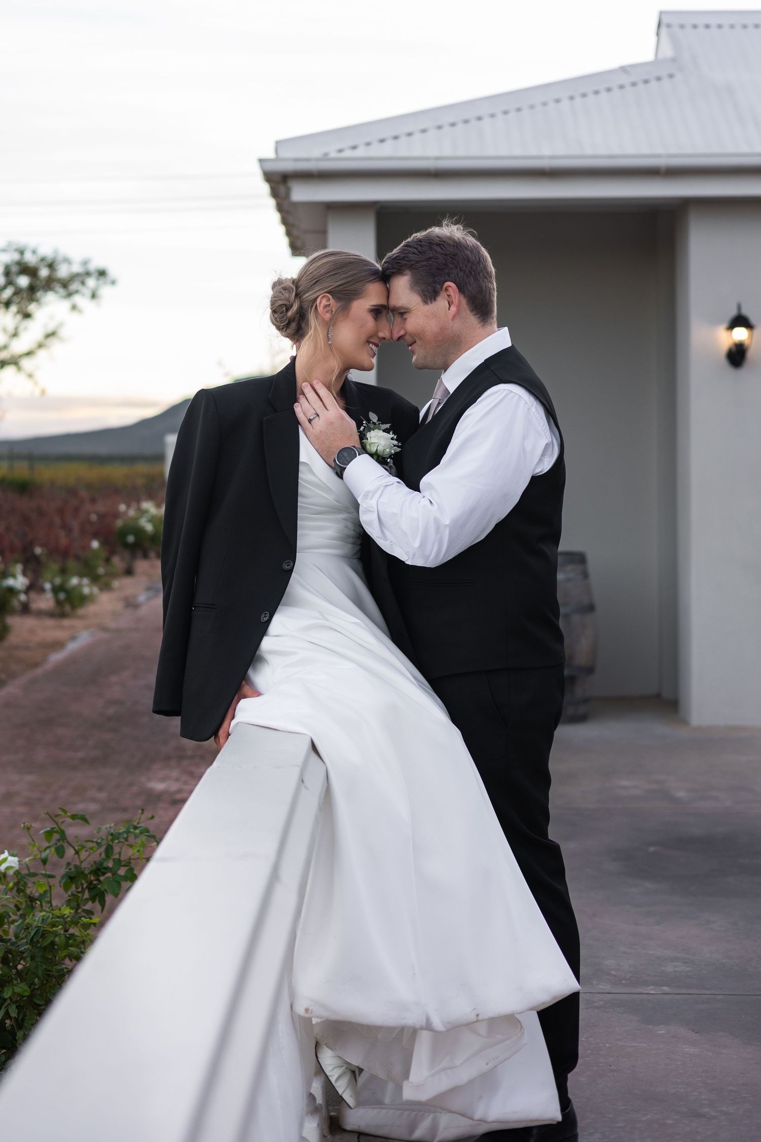 Bride and groom sharing a romantic moment leaning against a white balustrade at dusk.