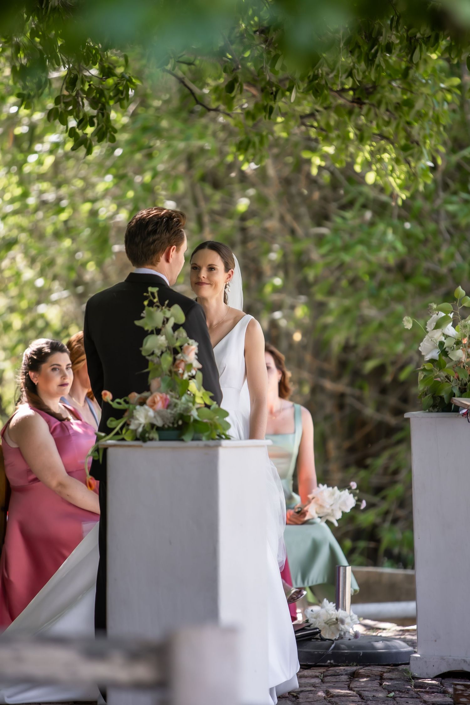Wedding reception setup with white planters and pink decor under natural garden setting.