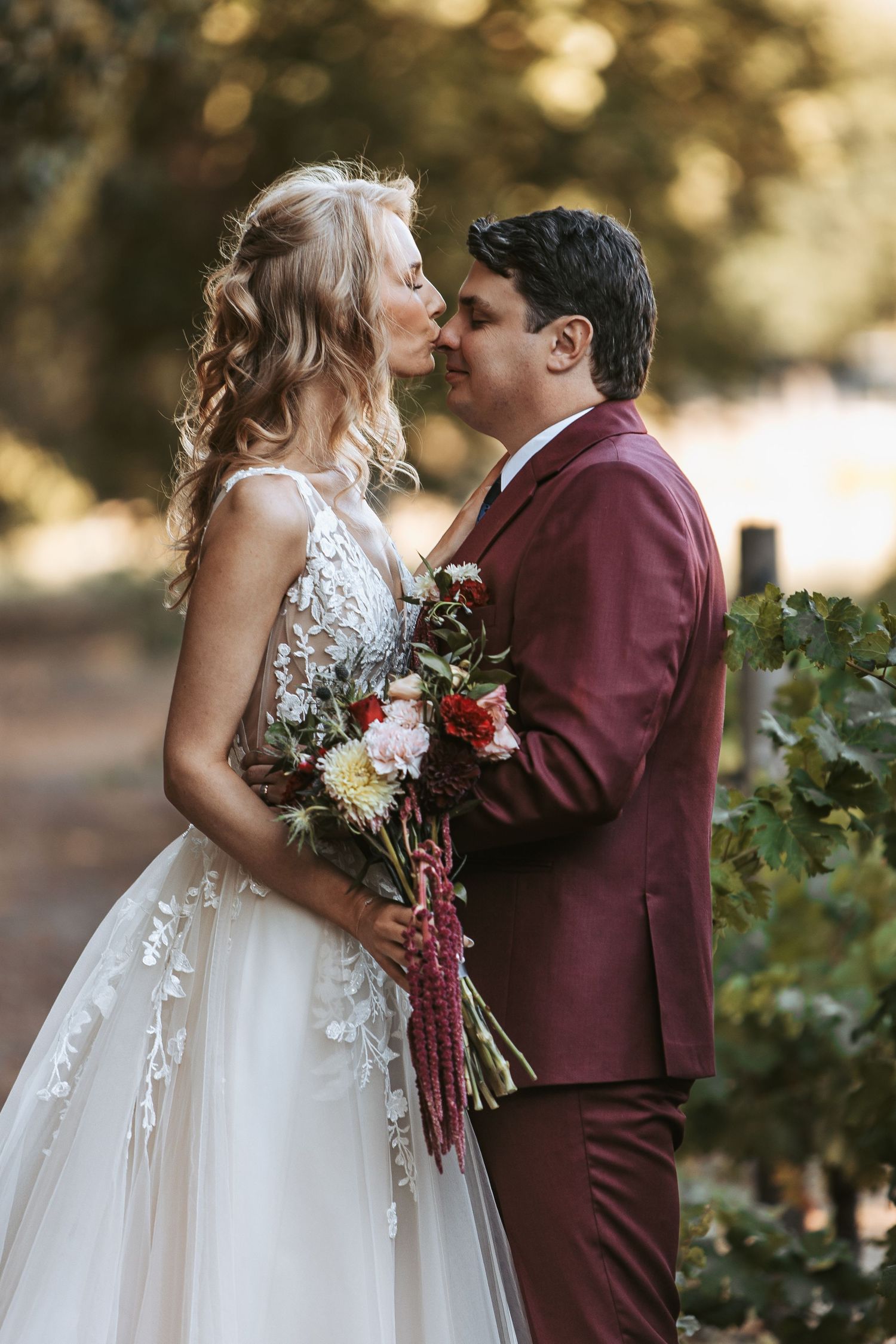 A romantic wedding photoshoot featuring a white gown and burgundy suit in an outdoor setting.
