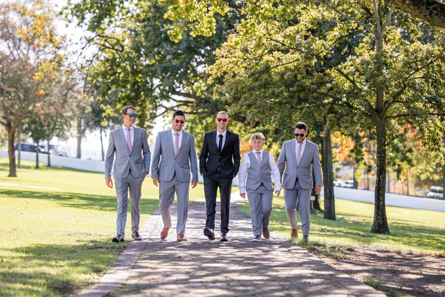 Wedding party walking together on a tree-lined path during autumn.