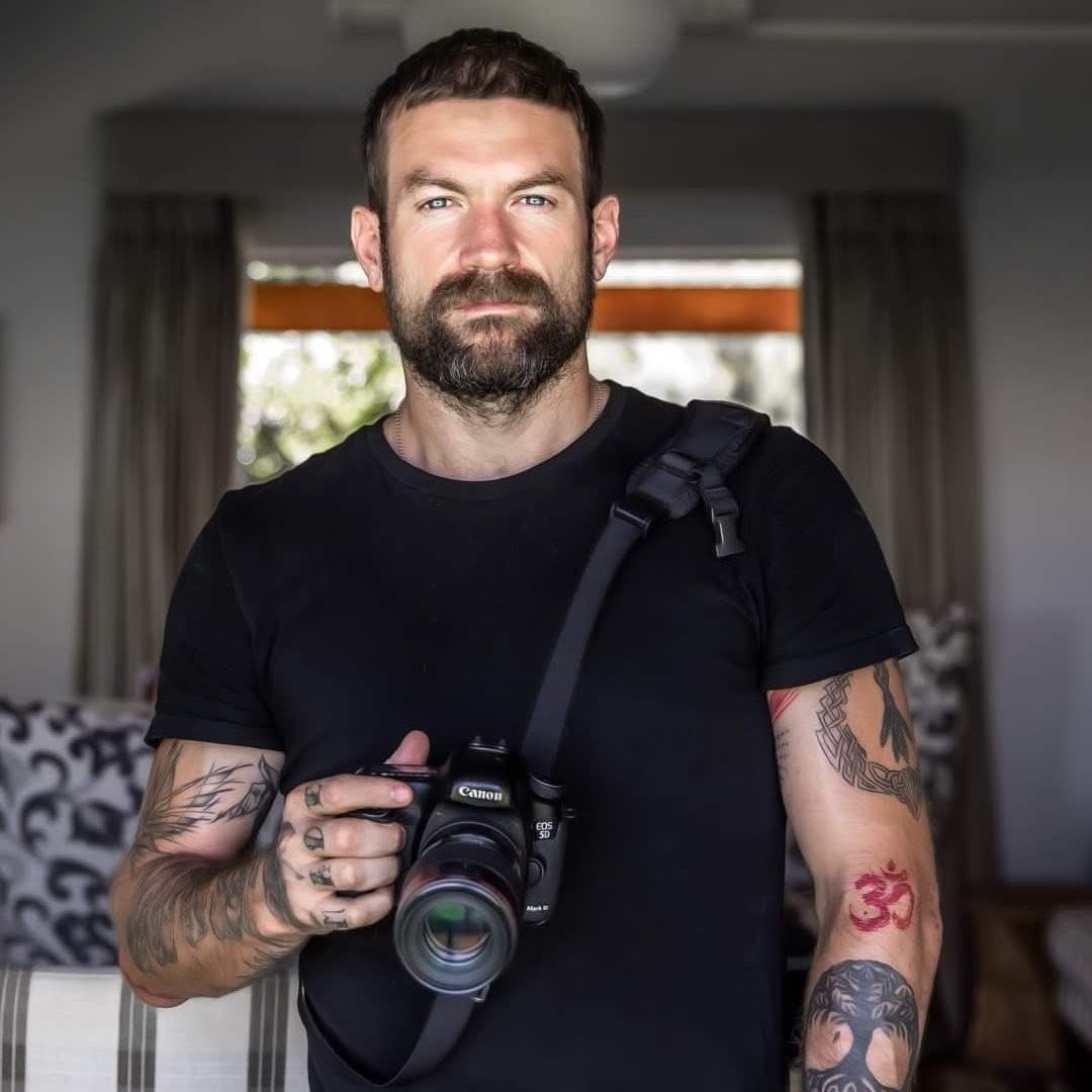 Professional photographer in black shirt holding camera equipment in modern indoor setting.