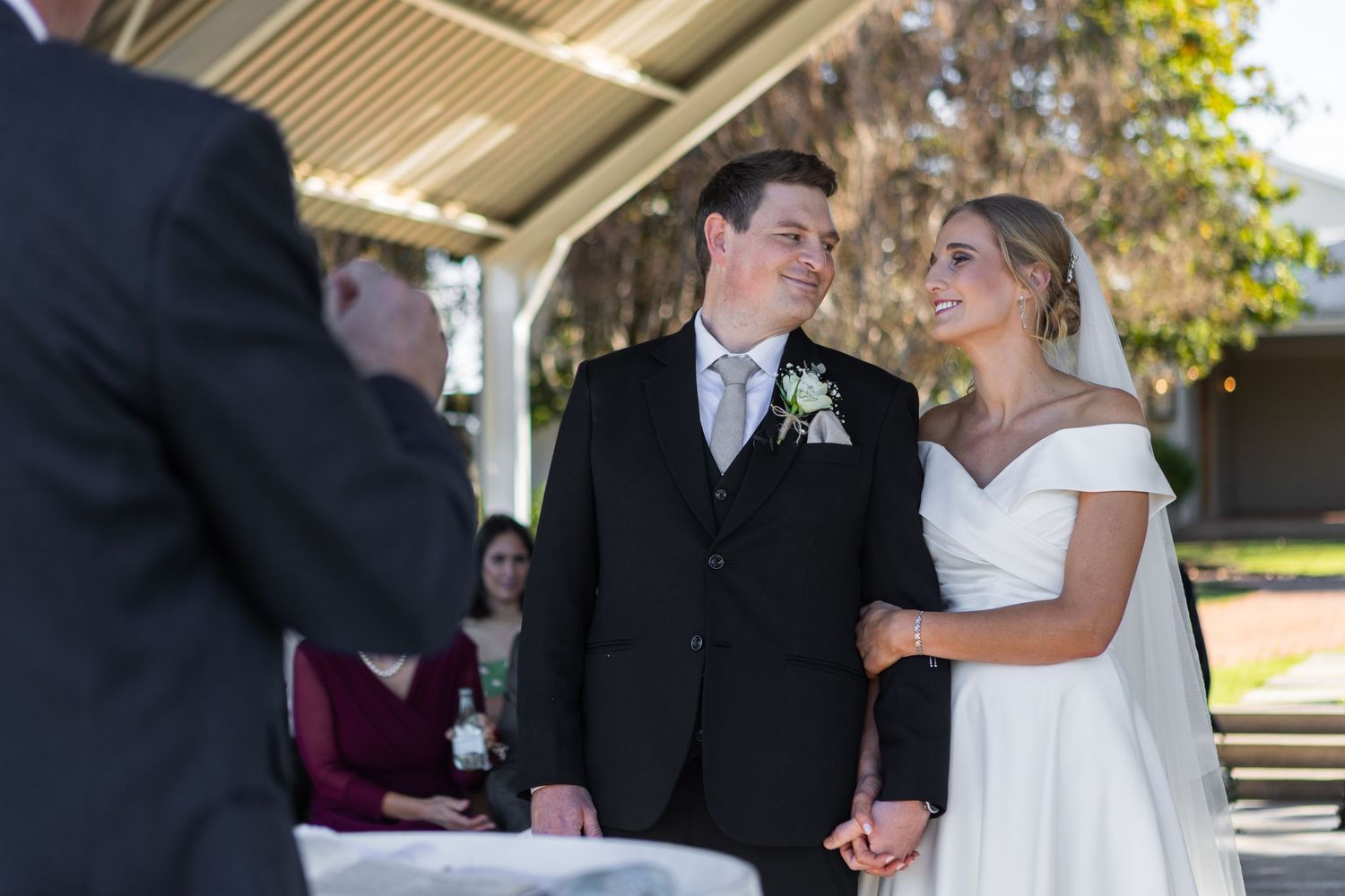 Bride and groom exchange vows outdoors under pavilion in classic wedding attire.
