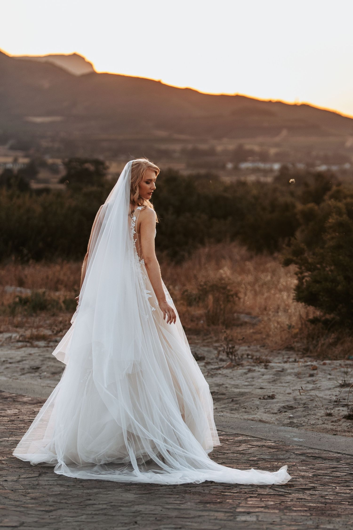 Ethereal bridal portrait featuring flowing white gown and veil against mountain landscape.