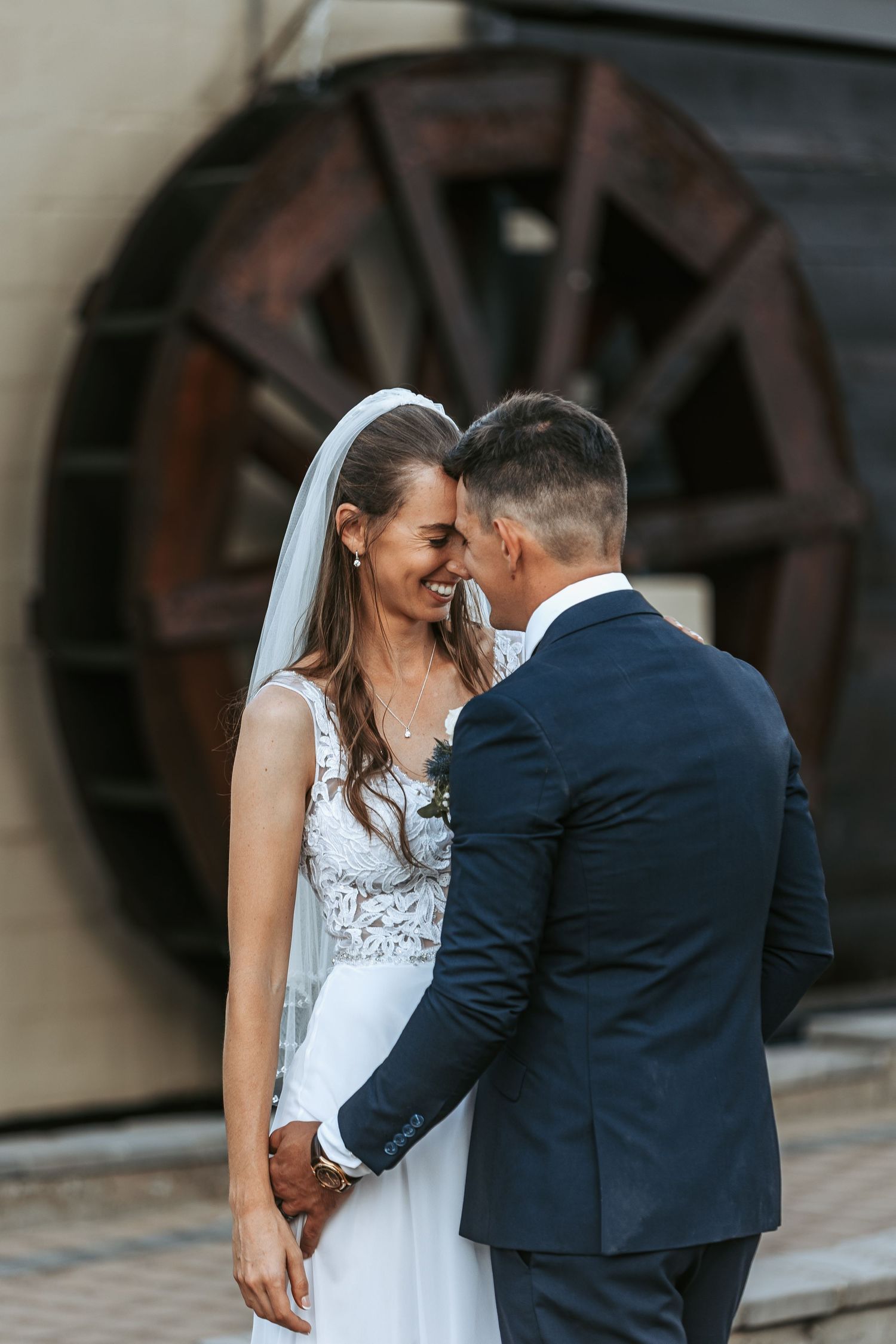 Wedding couple shares intimate moment near vintage wooden wheel backdrop.