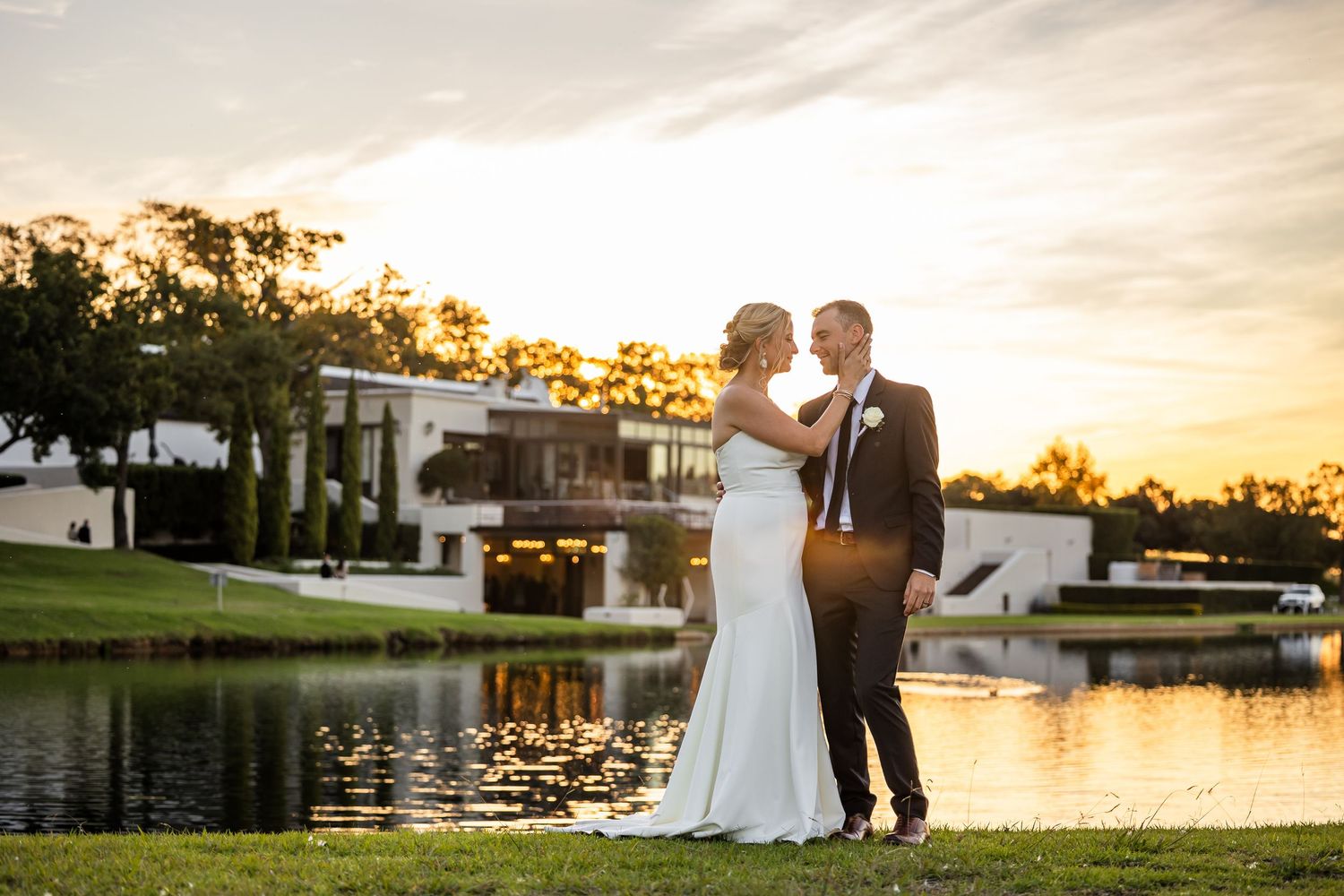 Wedding couple silhouetted against golden sunset by a waterfront during their outdoor ceremony.