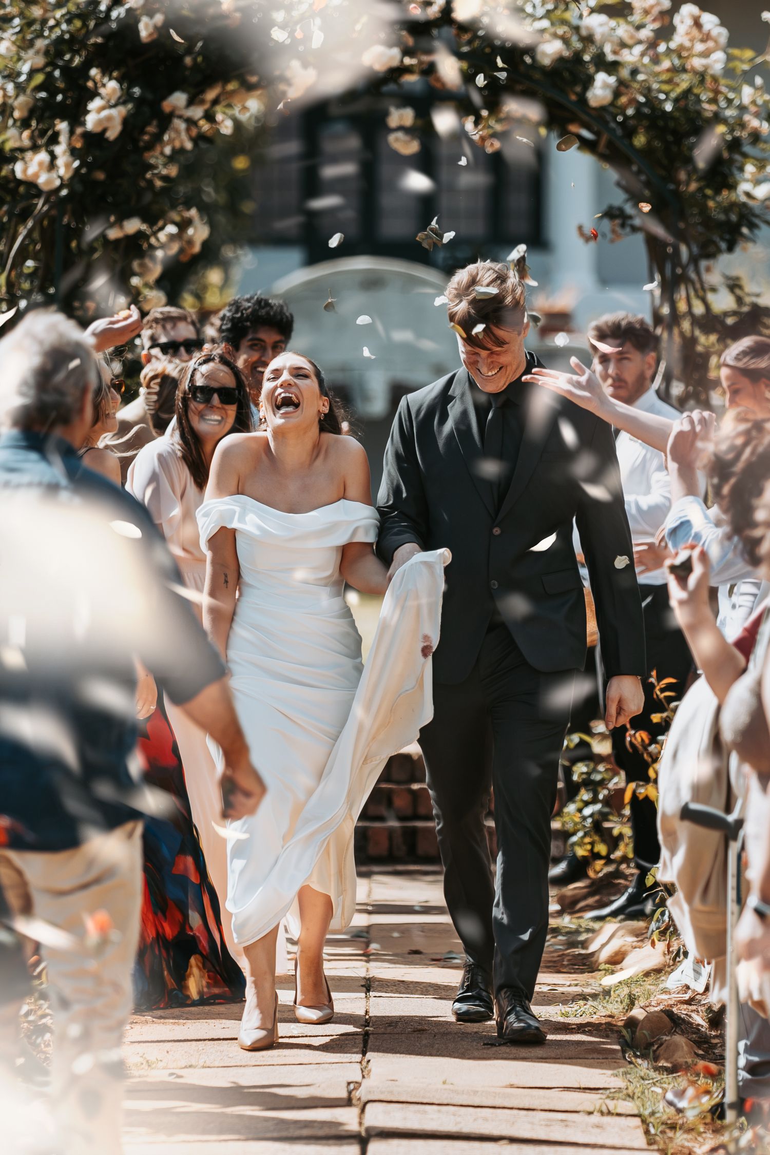 A group of people celebrate joyfully on a sunny day under blooming trees during an outdoor gathering.