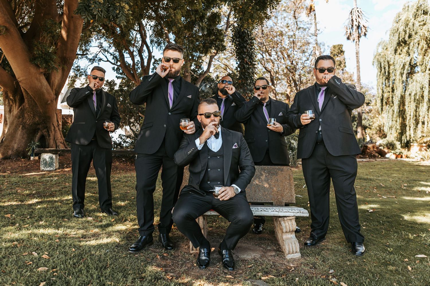Groomsmen laughing and celebrating together in formal attire at an outdoor wedding.