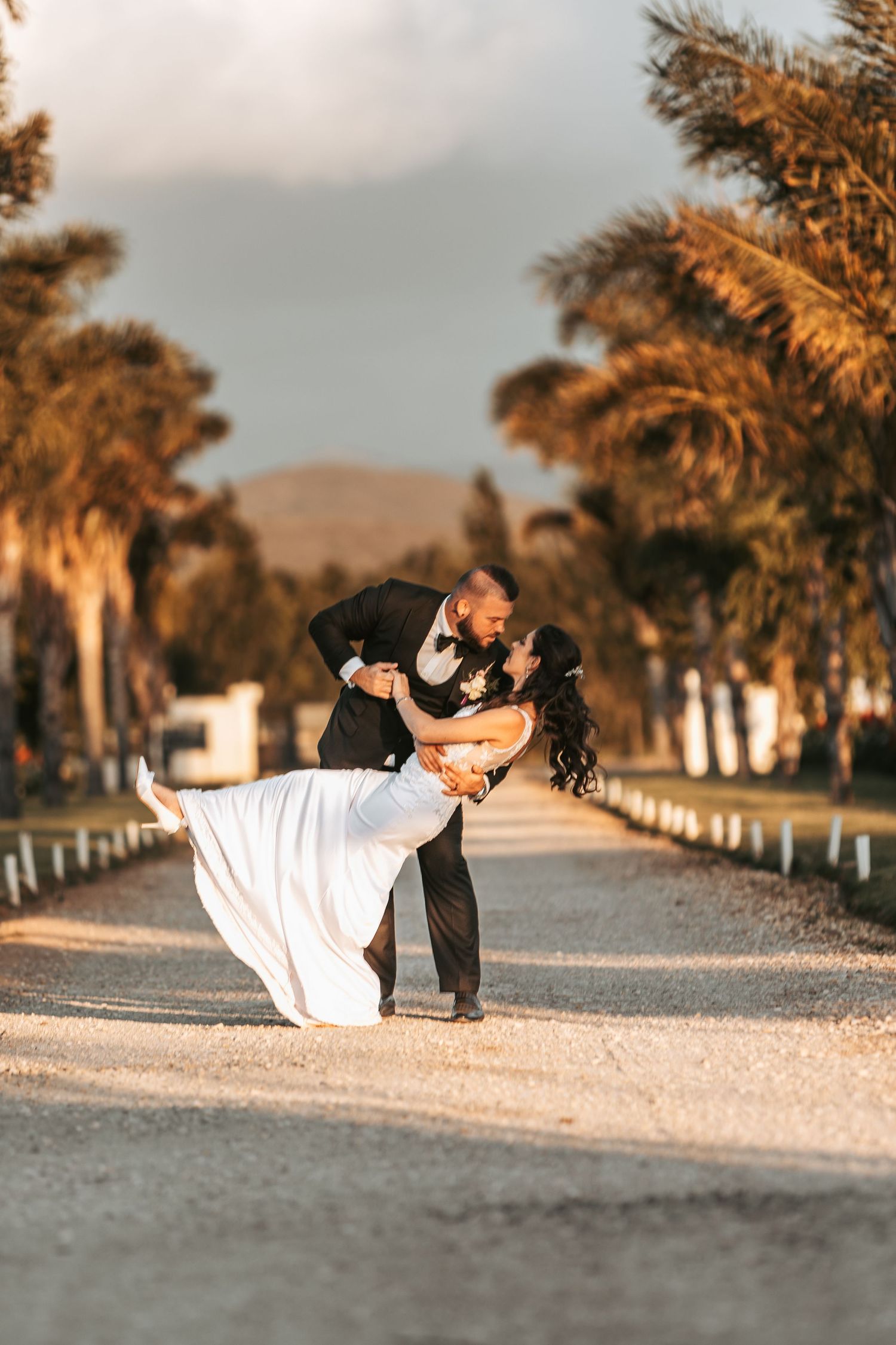 Dramatic wedding dance dip pose on a desert path with palm trees at golden hour.