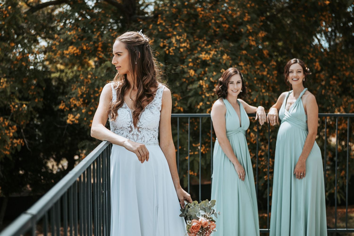 Wedding party in mint green dresses poses on outdoor balcony with autumn foliage.