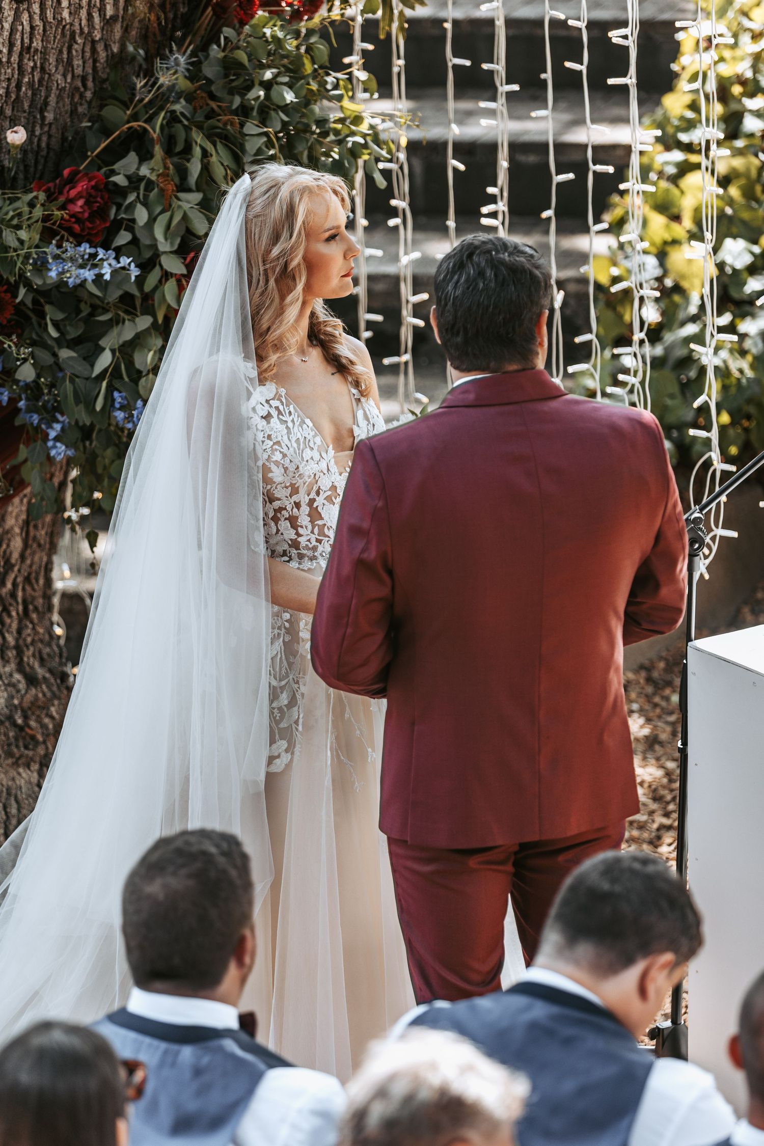An intimate wedding ceremony moment under string lights and trees with guests looking on.