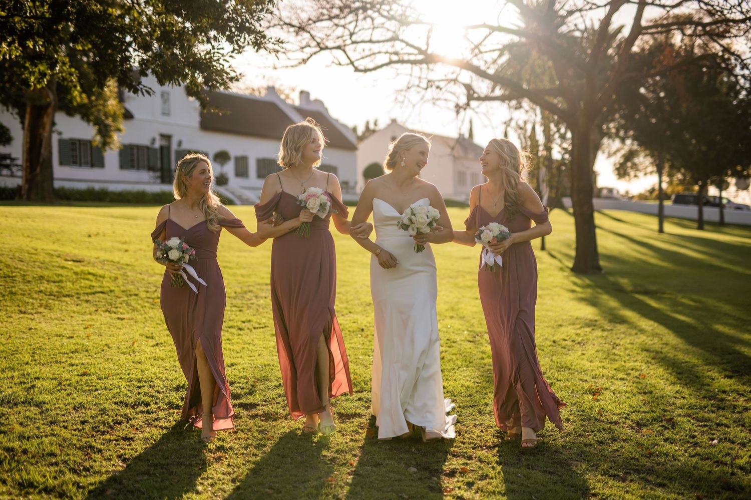 Wedding party celebrating at sunset in a grassy field with golden backlighting.
