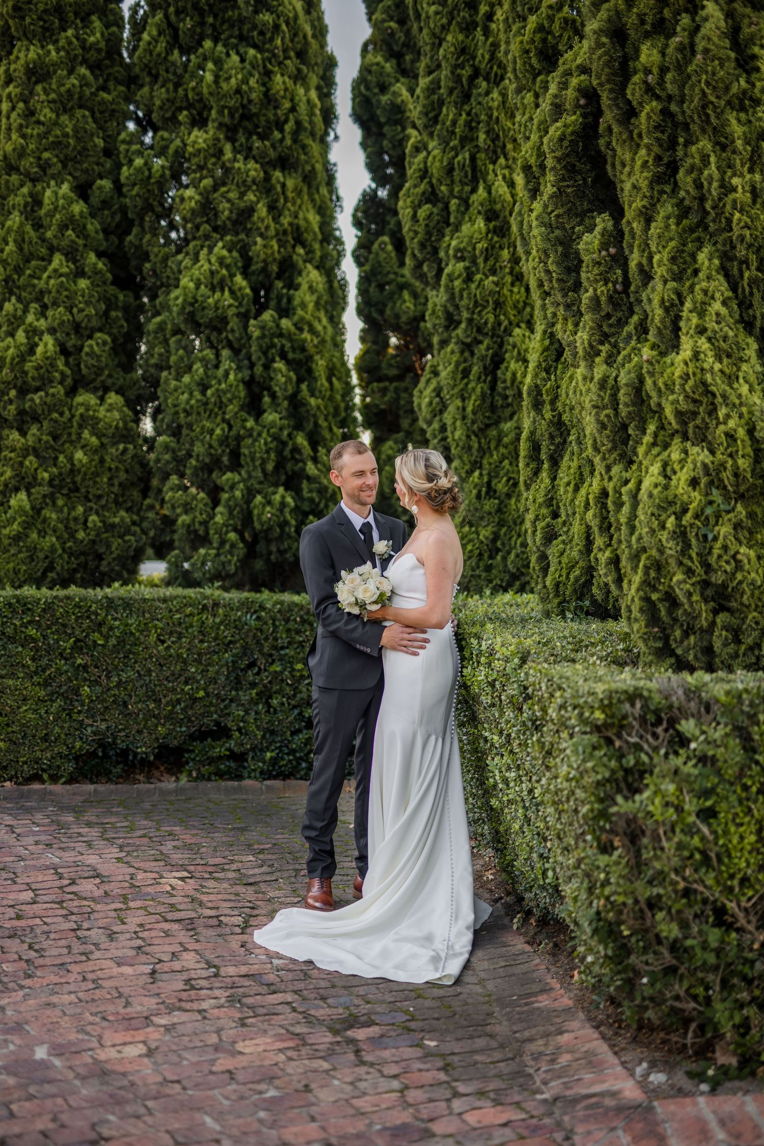 Romantic wedding photos taken against a backdrop of tall cypress trees and brick pathway.