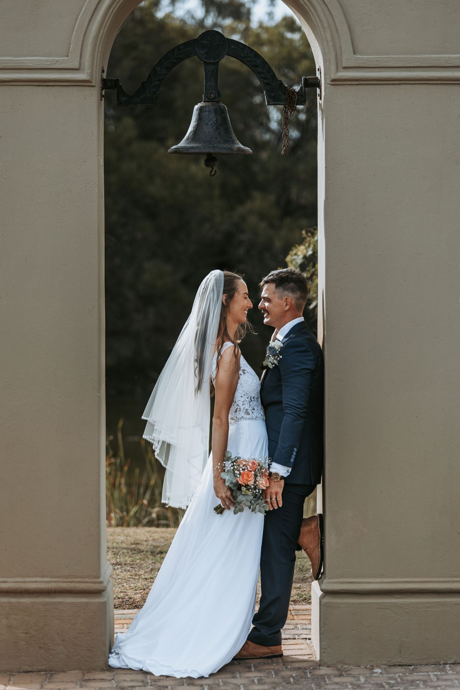 Romantic wedding portrait under an elegant archway at outdoor venue.