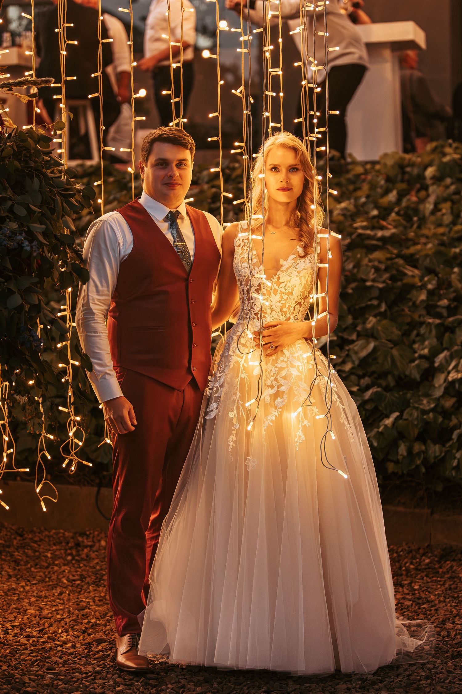 A couple illuminated by hanging fairy lights creates a magical wedding portrait at night.