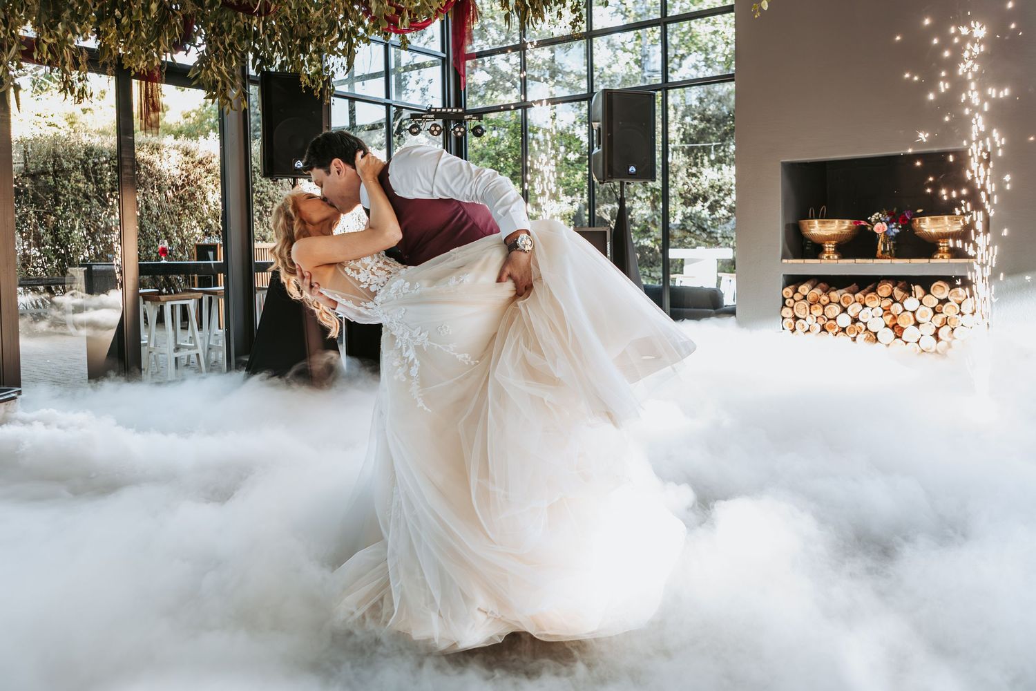 A bride and groom share their first dance on a misty dance floor with twinkling lights in the background.