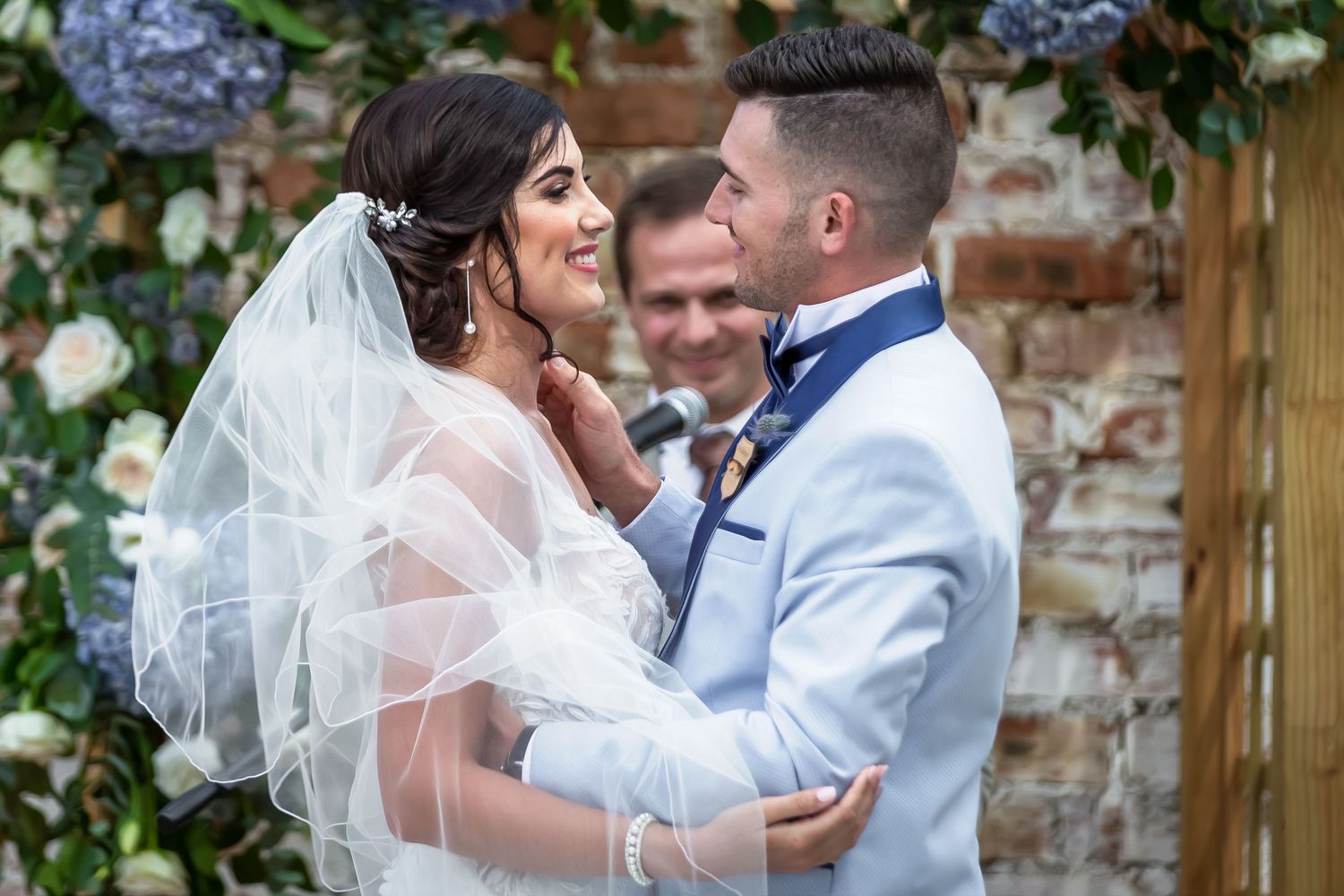 Joyful wedding couple sharing intimate moments in a garden setting with brick walls and greenery in the background.