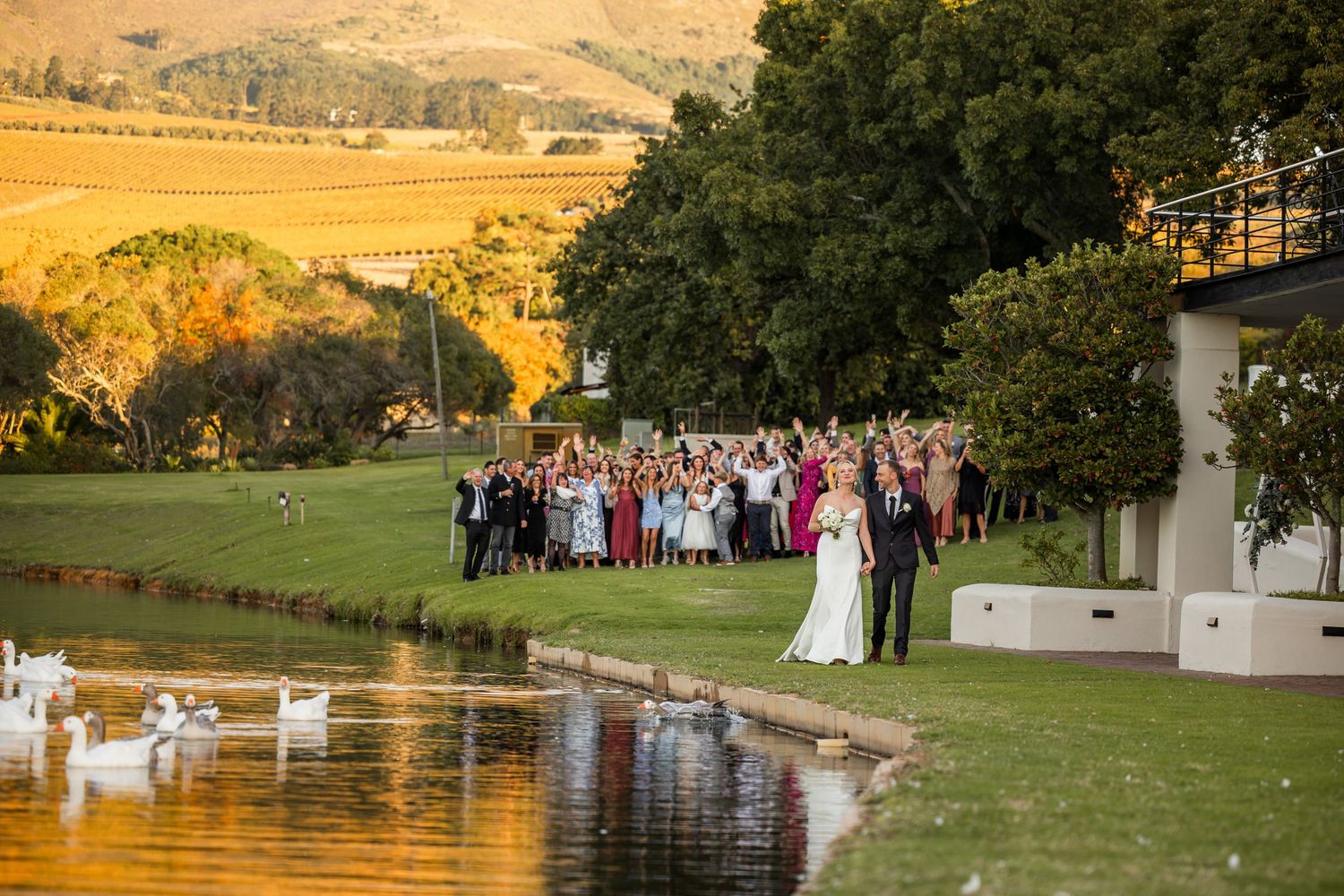 Large wedding group photo being taken outdoors with scenic countryside views.