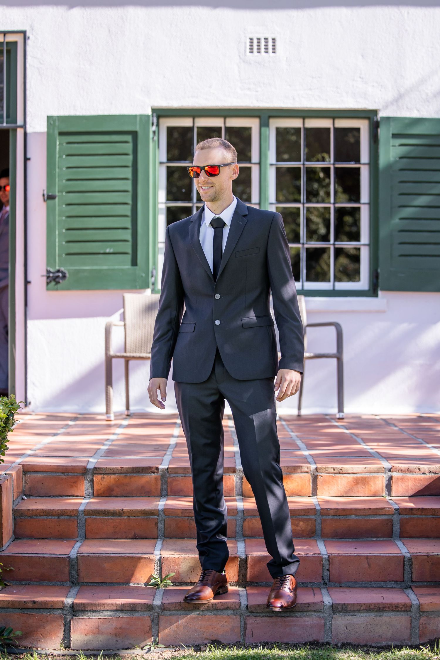 Sequence showing legs in dress shoes walking down brick steps with green shuttered windows in background.