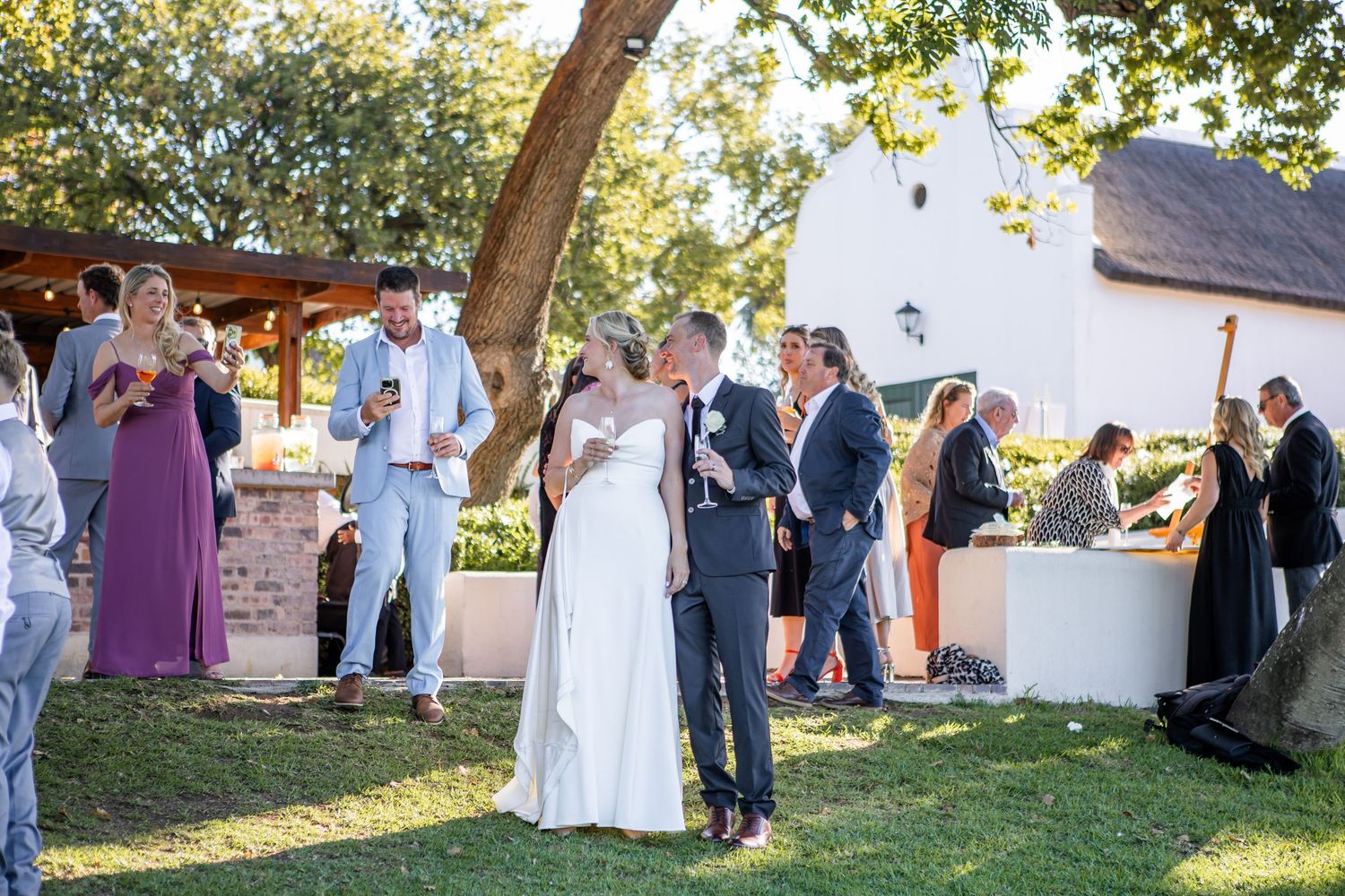 Outdoor wedding reception with guests mingling on a lawn during golden hour.