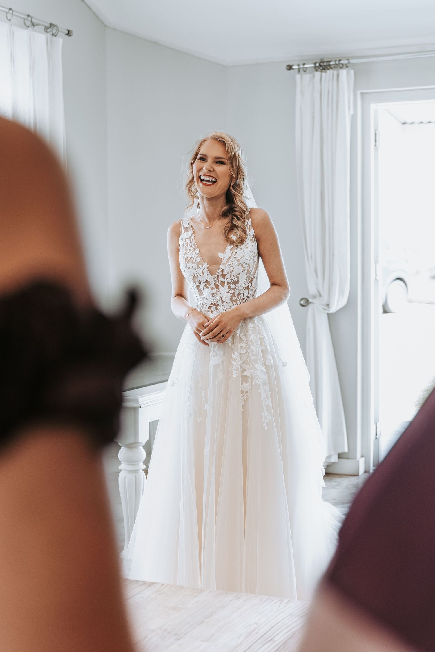 Natural light portrait of bride laughing in elegant white lace wedding dress.